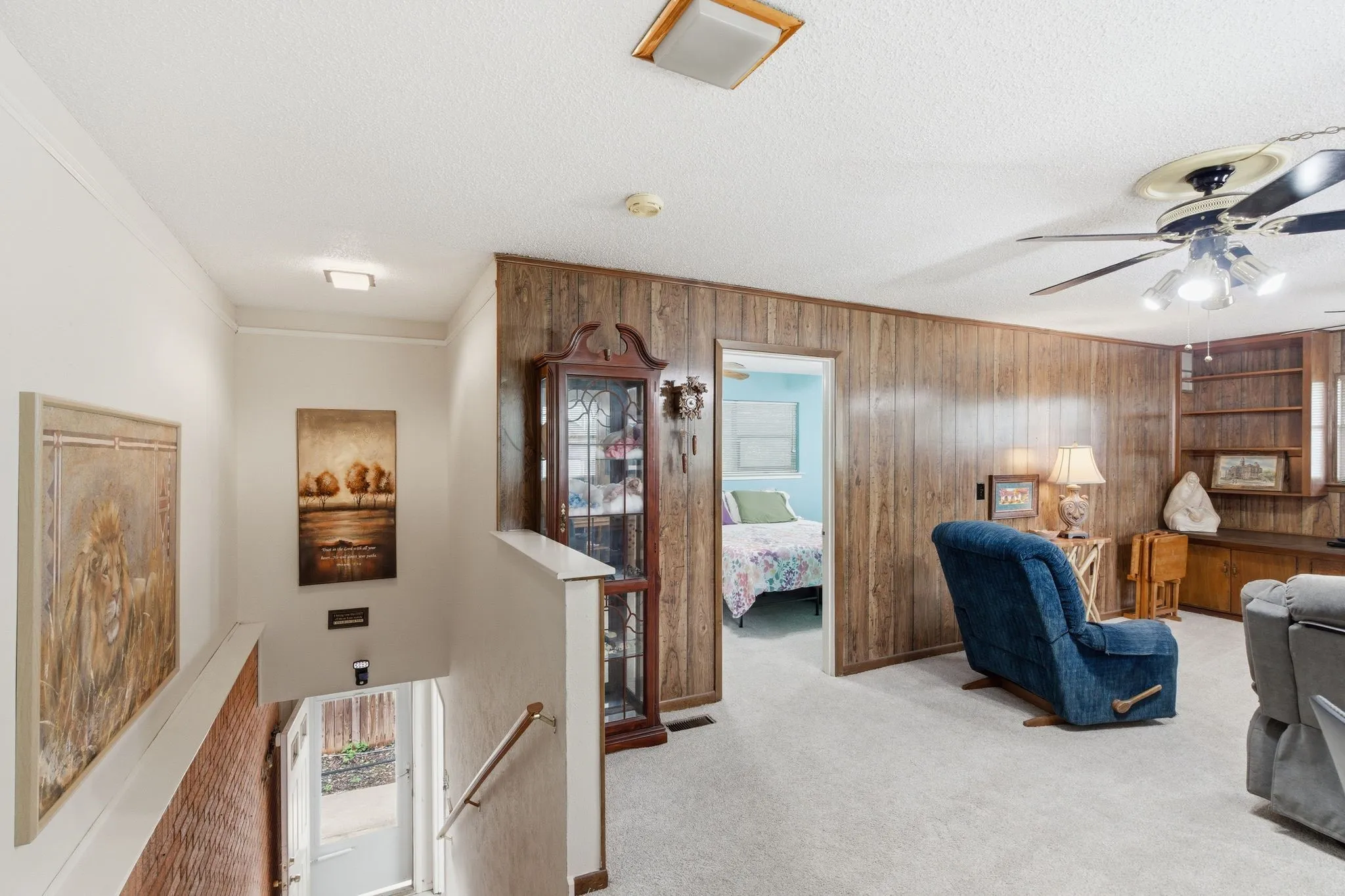 Carpeted living area featuring wood-paneled walls and a ceiling fan