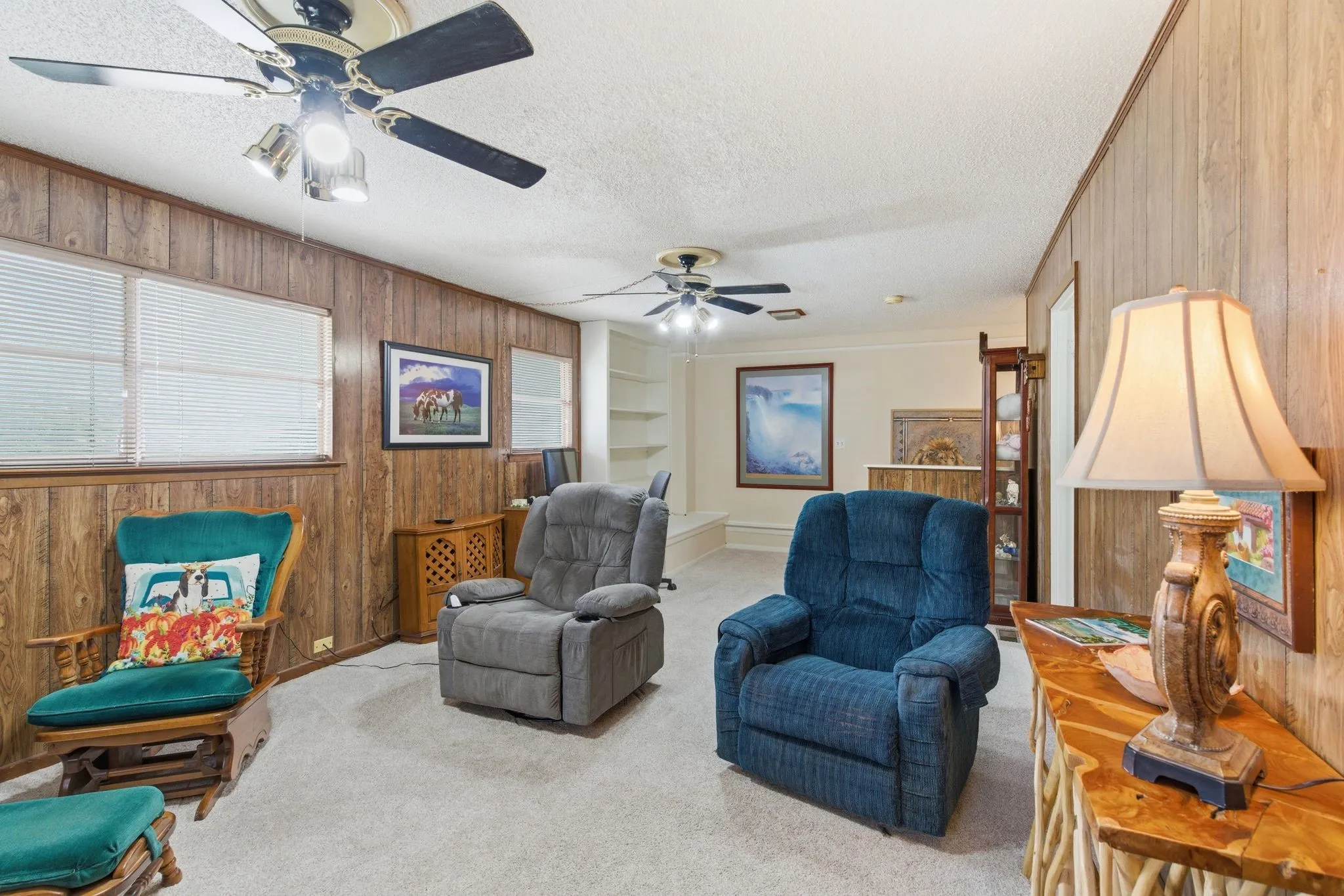 Room featuring wood-finish paneling, light-colored carpet, and multiple windows with blinds