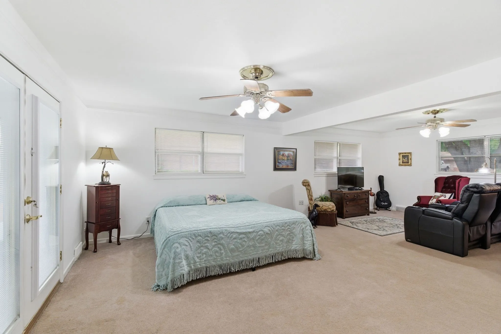 Spacious room with plush carpet flooring, multiple windows, and two ceiling fans