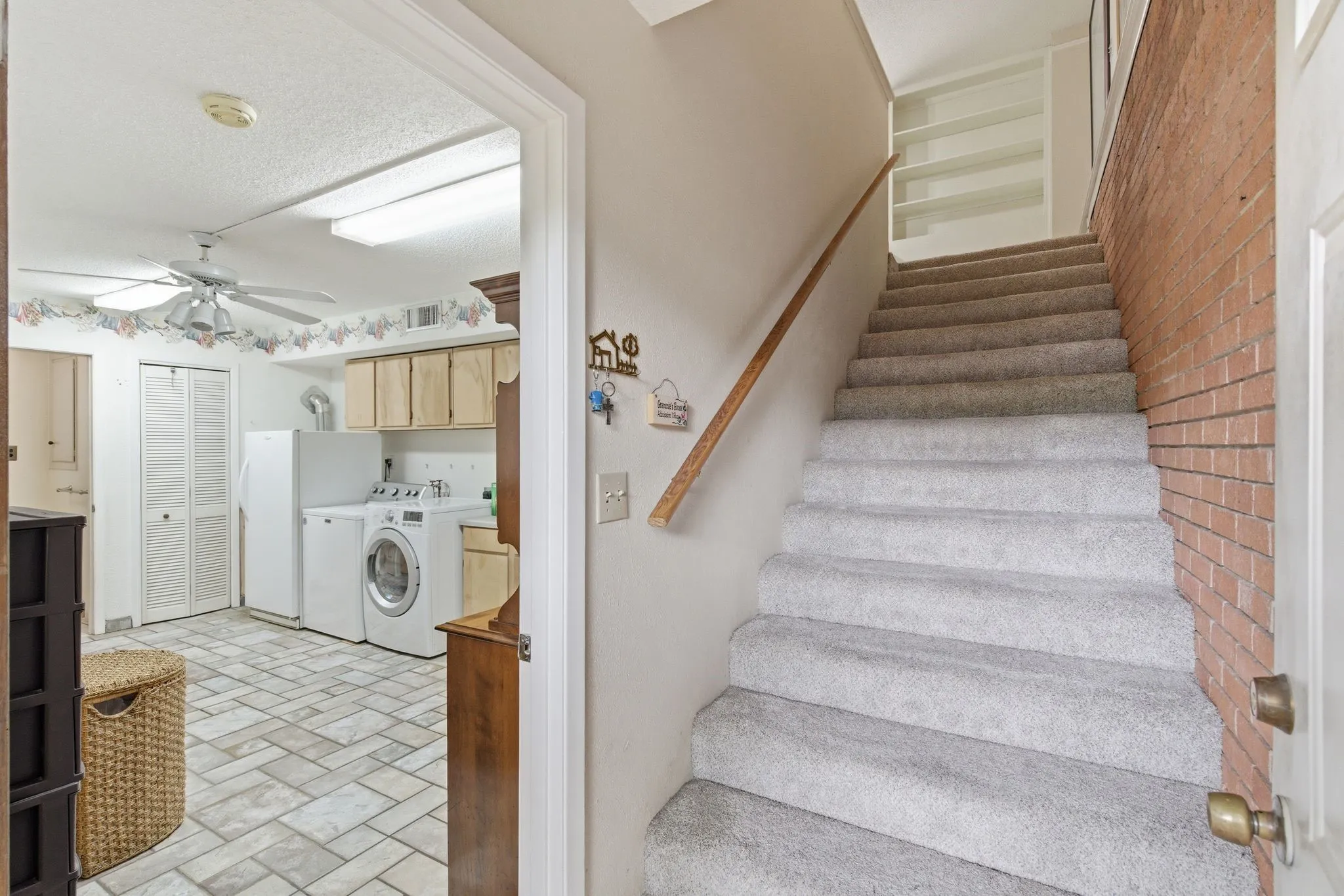 Carpeted staircase with wooden handrail and exposed brick wall