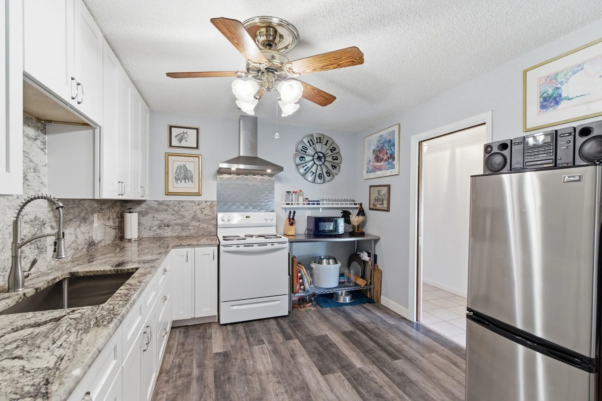 Kitchen featuring wood-finish flooring, white cabinetry, a stainless steel refrigerator, and a stainless steel sink with a pull-down faucet