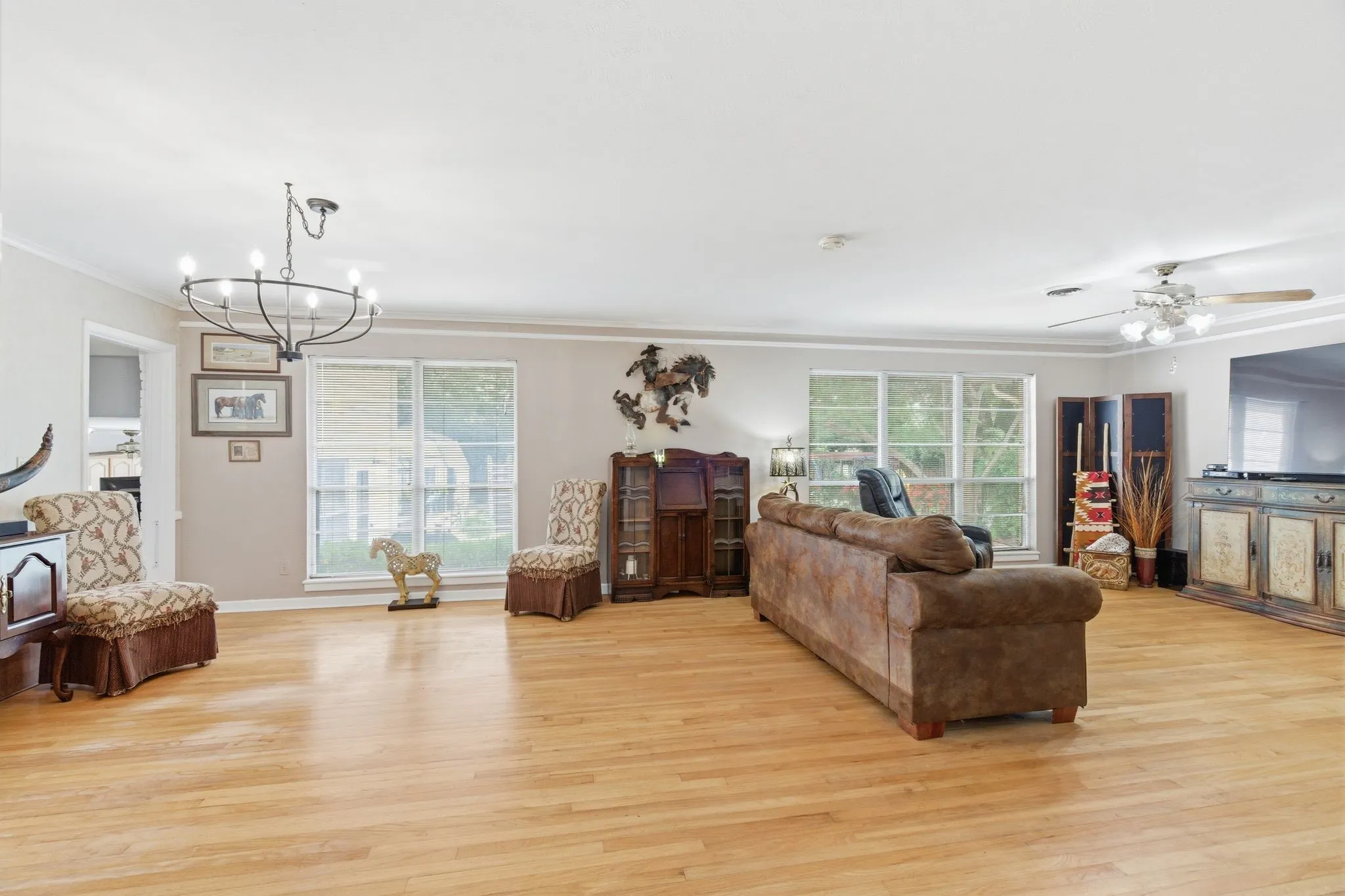 Spacious living area featuring light wood-finish flooring, multiple windows, a ceiling fan, and a chandelier