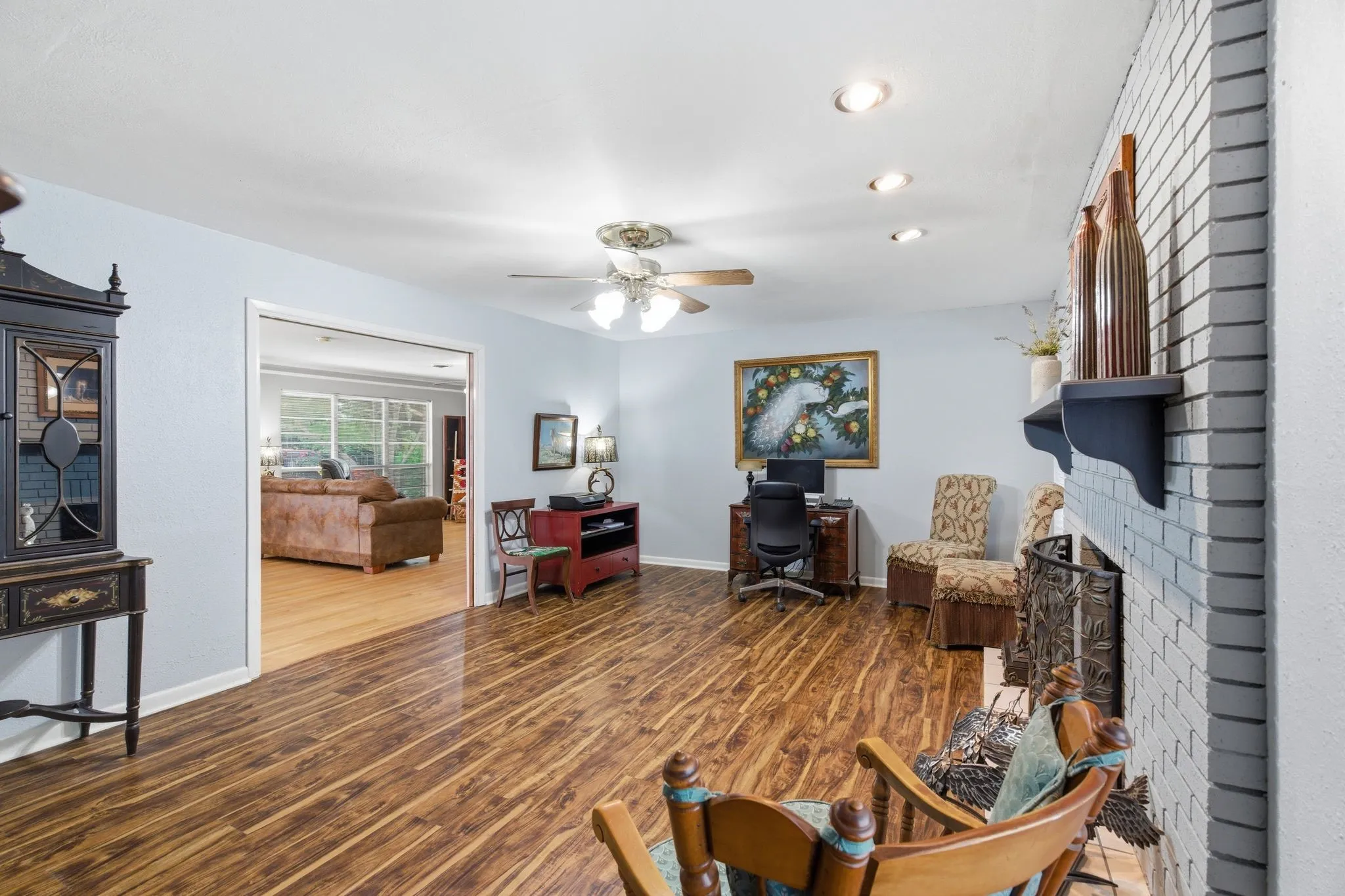 Spacious interior featuring wood-finish flooring, a painted brick fireplace with mantel, recessed lighting, and a ceiling fan