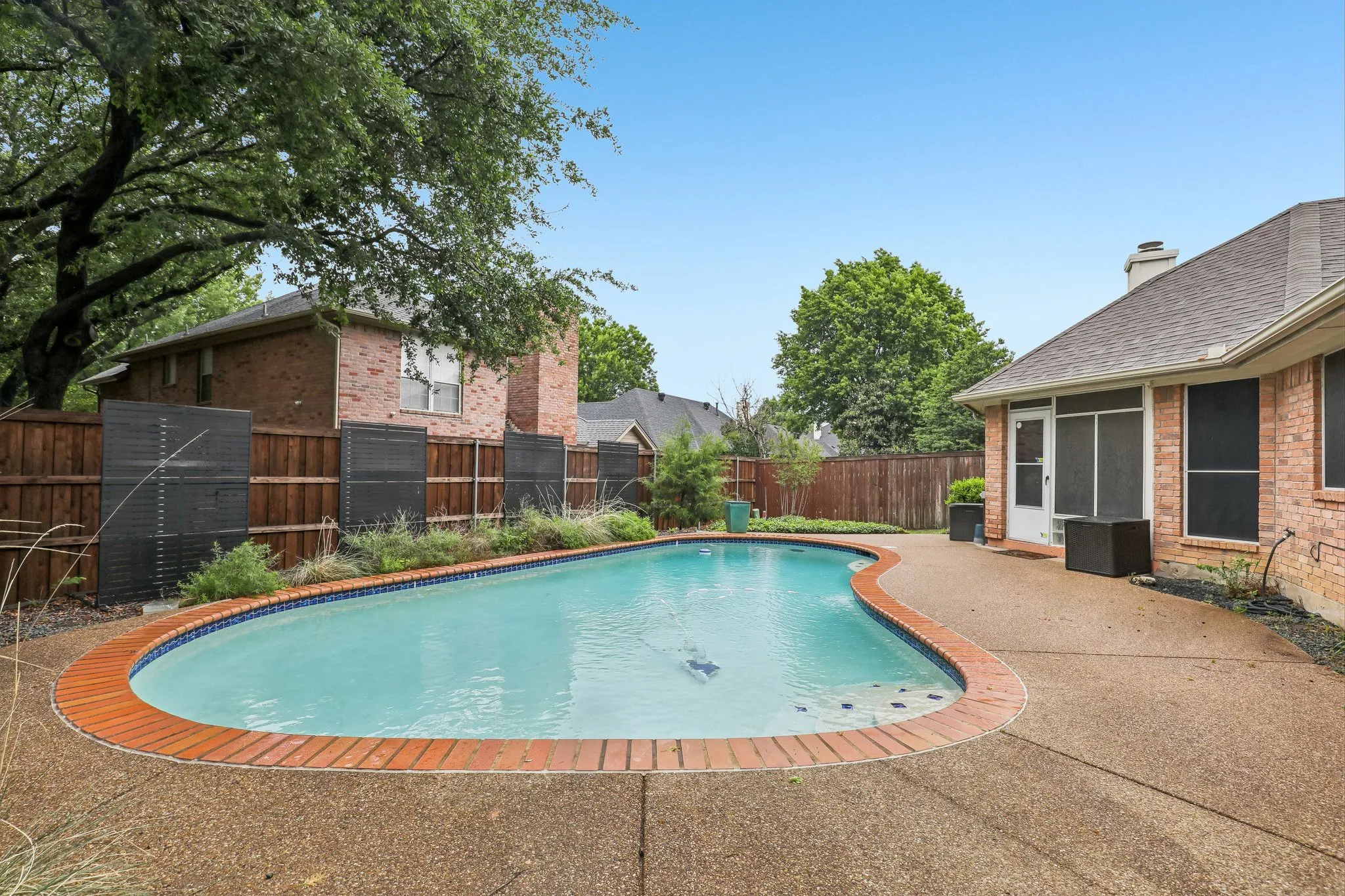 Curved swimming pool with brick coping and exposed aggregate concrete decking