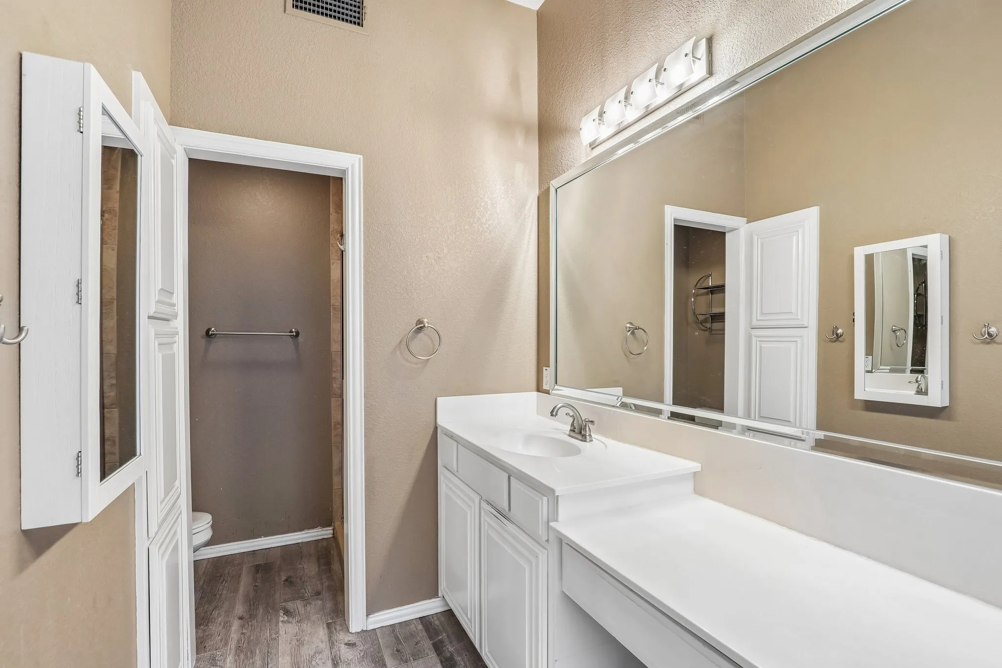 Bathroom featuring an expansive vanity with an integrated sink, white cabinetry, and a full-width mirror