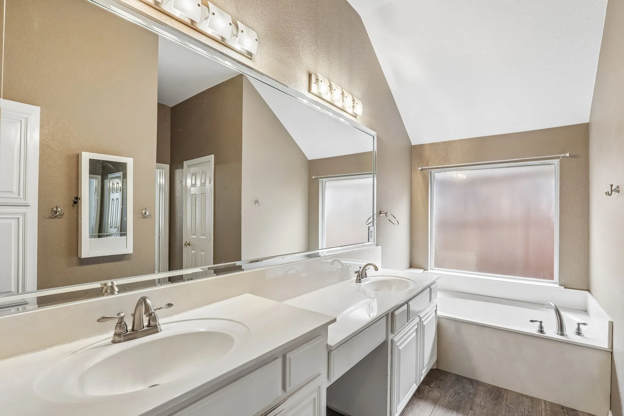 Spacious bathroom featuring a double vanity with white cabinetry, integrated sinks, and brushed nickel faucets