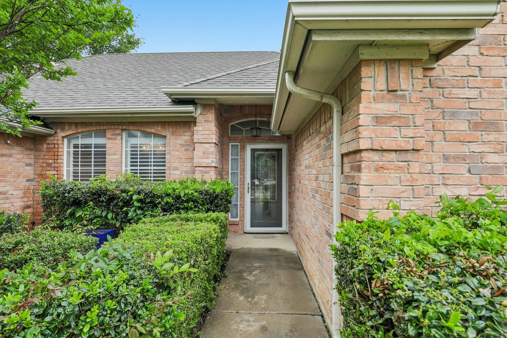 Brick facade home featuring a gabled roof, white gutters, and a covered entry