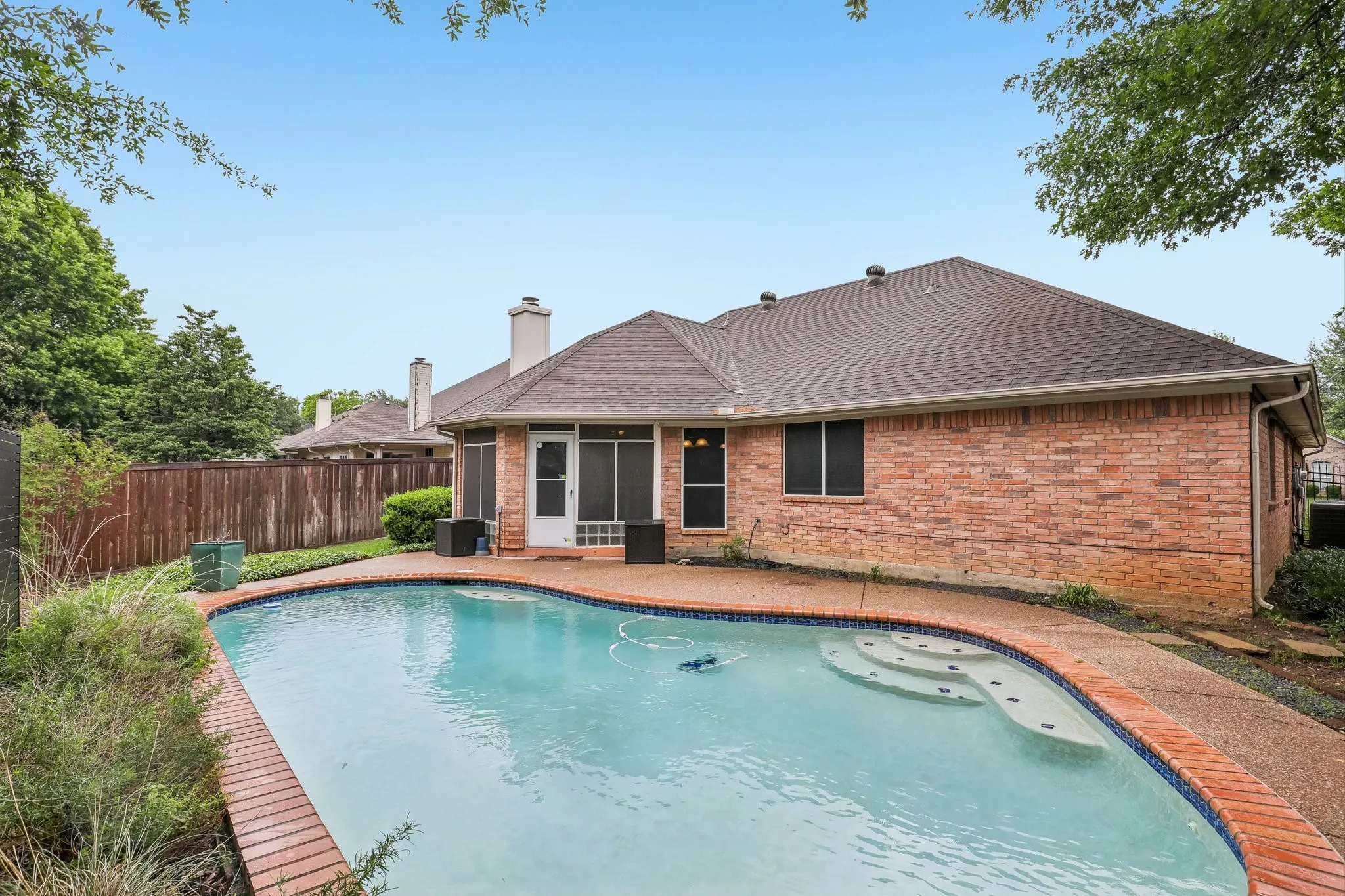 Curved swimming pool with integrated steps, brick coping, and surrounding concrete deck