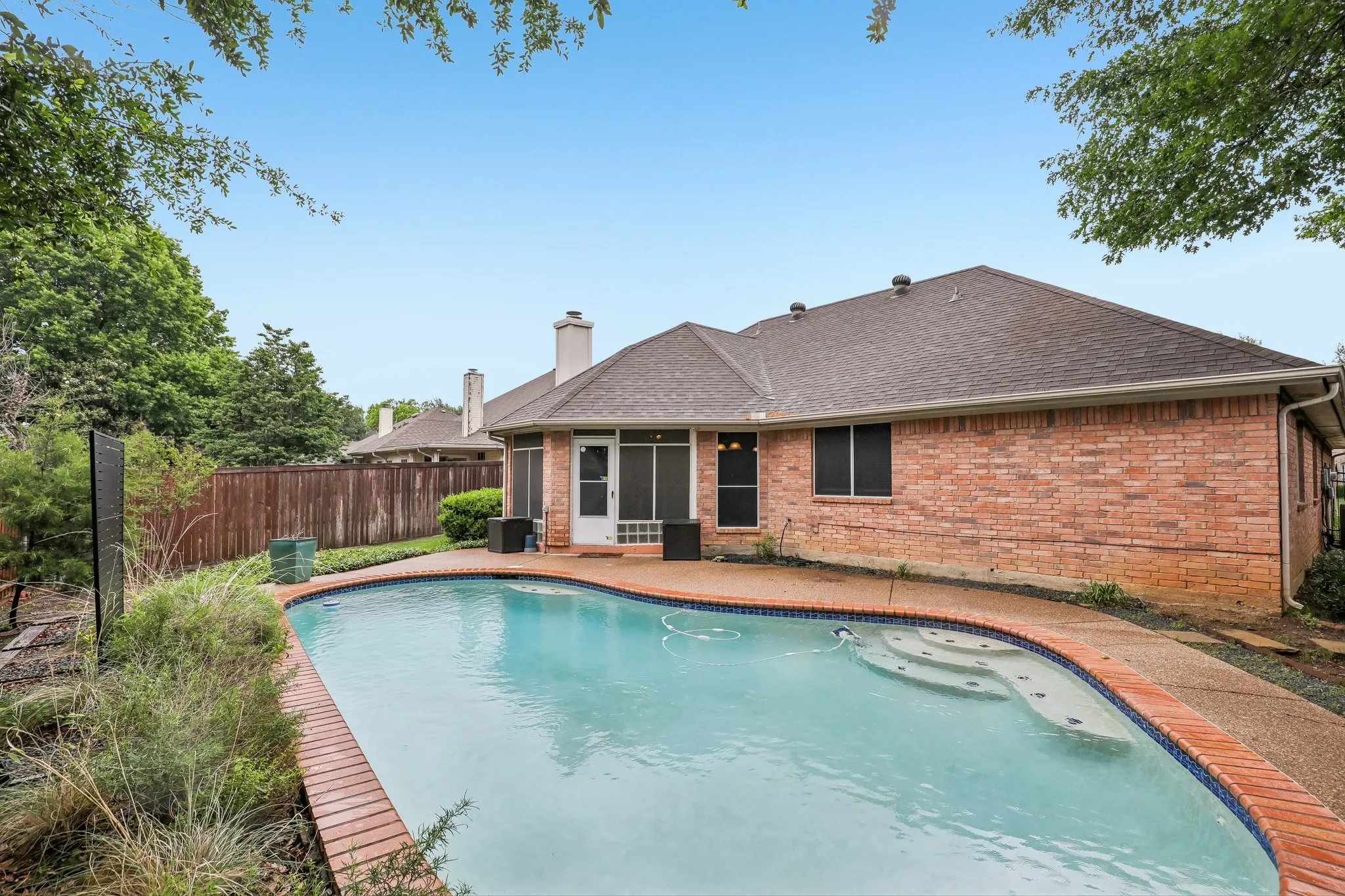 Curved swimming pool featuring an integrated spa, brick coping, and a textured concrete deck