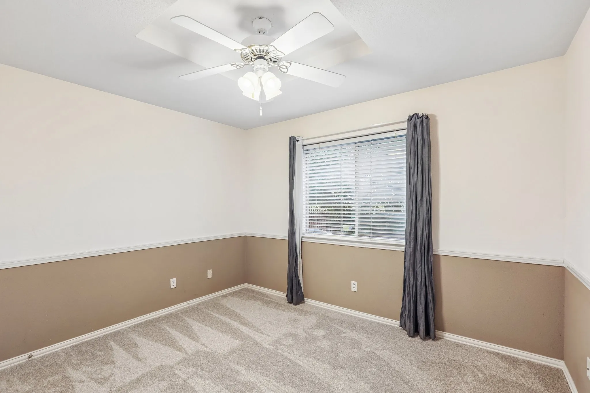 Interior room featuring neutral-toned walls with a two-tone paint treatment, a ceiling fan with integrated lighting, a window with horizontal blinds, and grey carpeting
