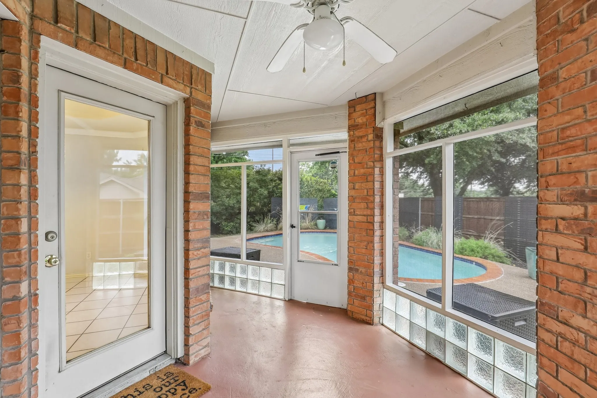Screened porch featuring brick accents, overhead ceiling fan, and access to a curvilinear swimming pool