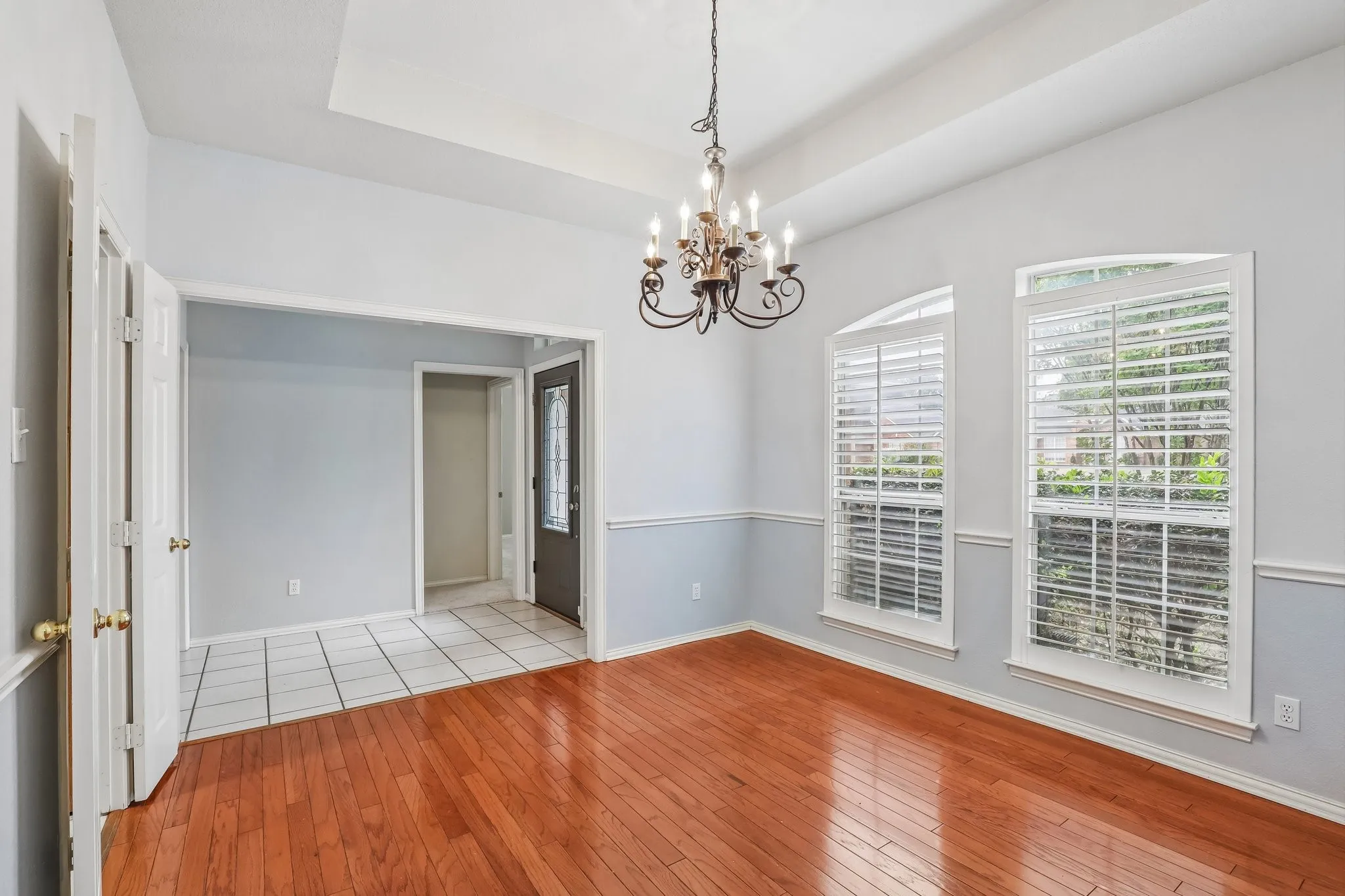 Spacious room featuring wood-finish flooring, a tray ceiling, and a chandelier