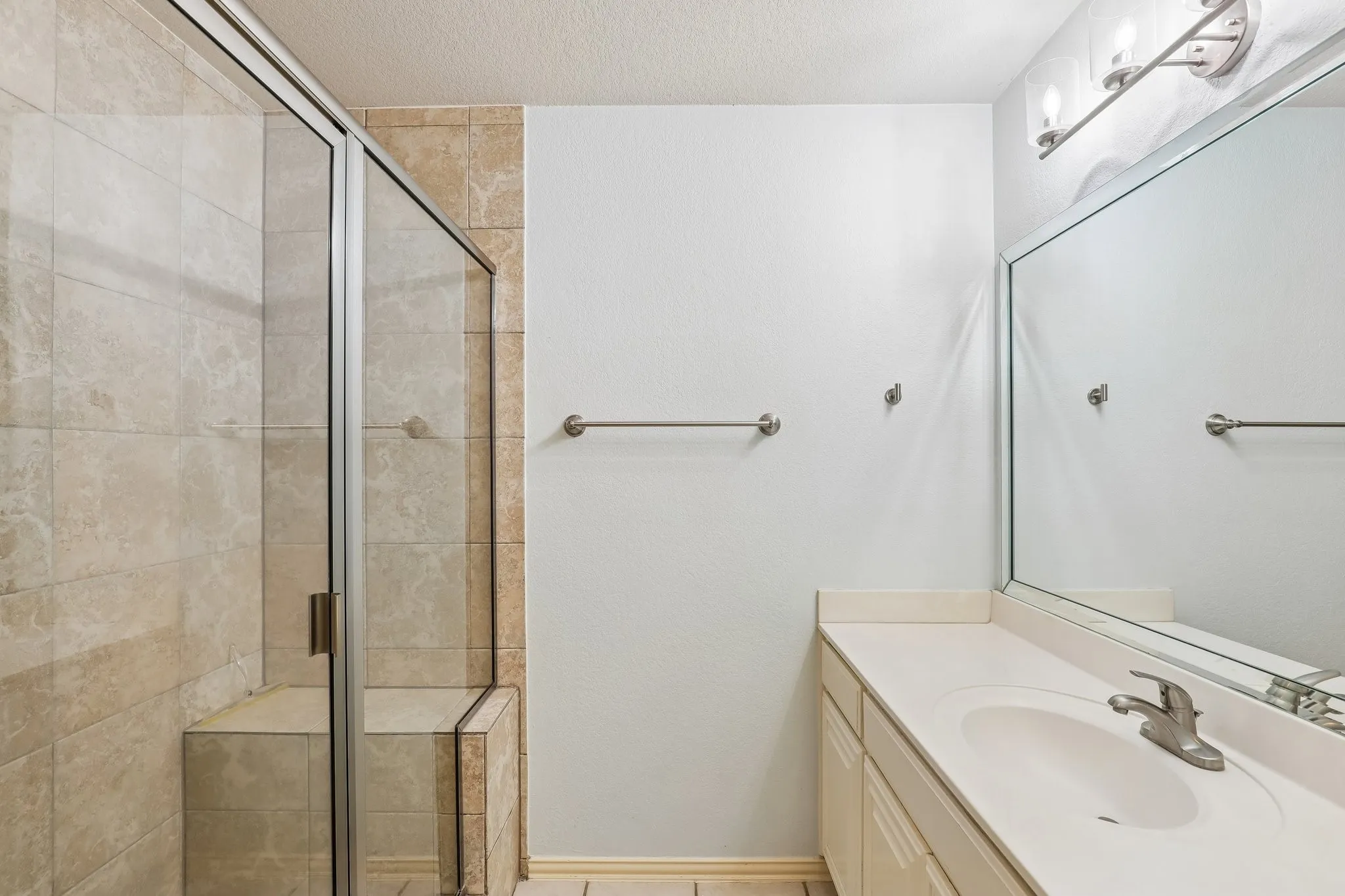 Bathroom featuring a glass-enclosed shower with a built-in bench and large format wall tiles, vanity with an integrated sink, and a large mirror with overhead lighting