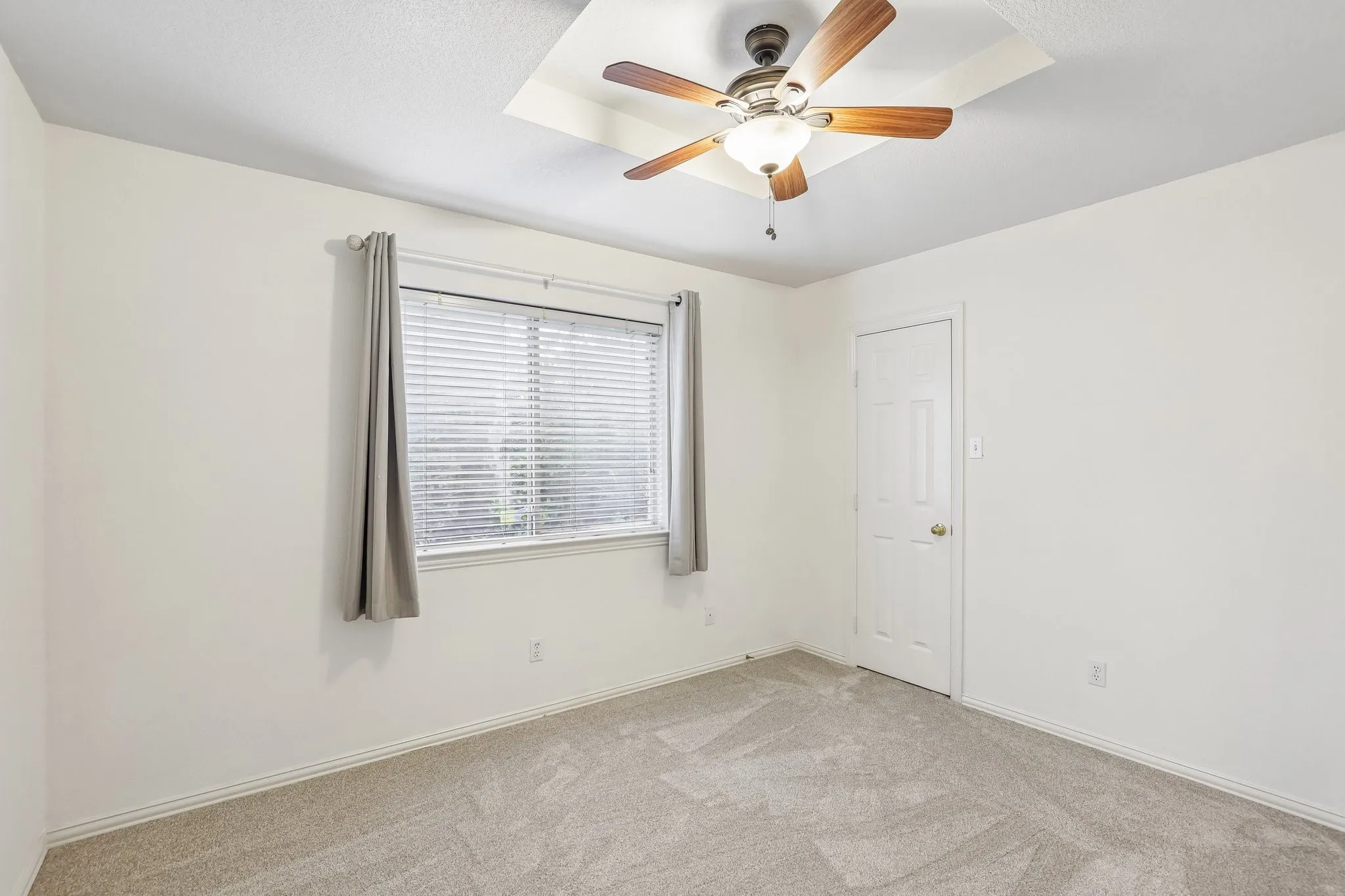 Recessed ceiling detail with a wood-finish ceiling fan, neutral wall paint, window with blinds, and light-toned carpeting
