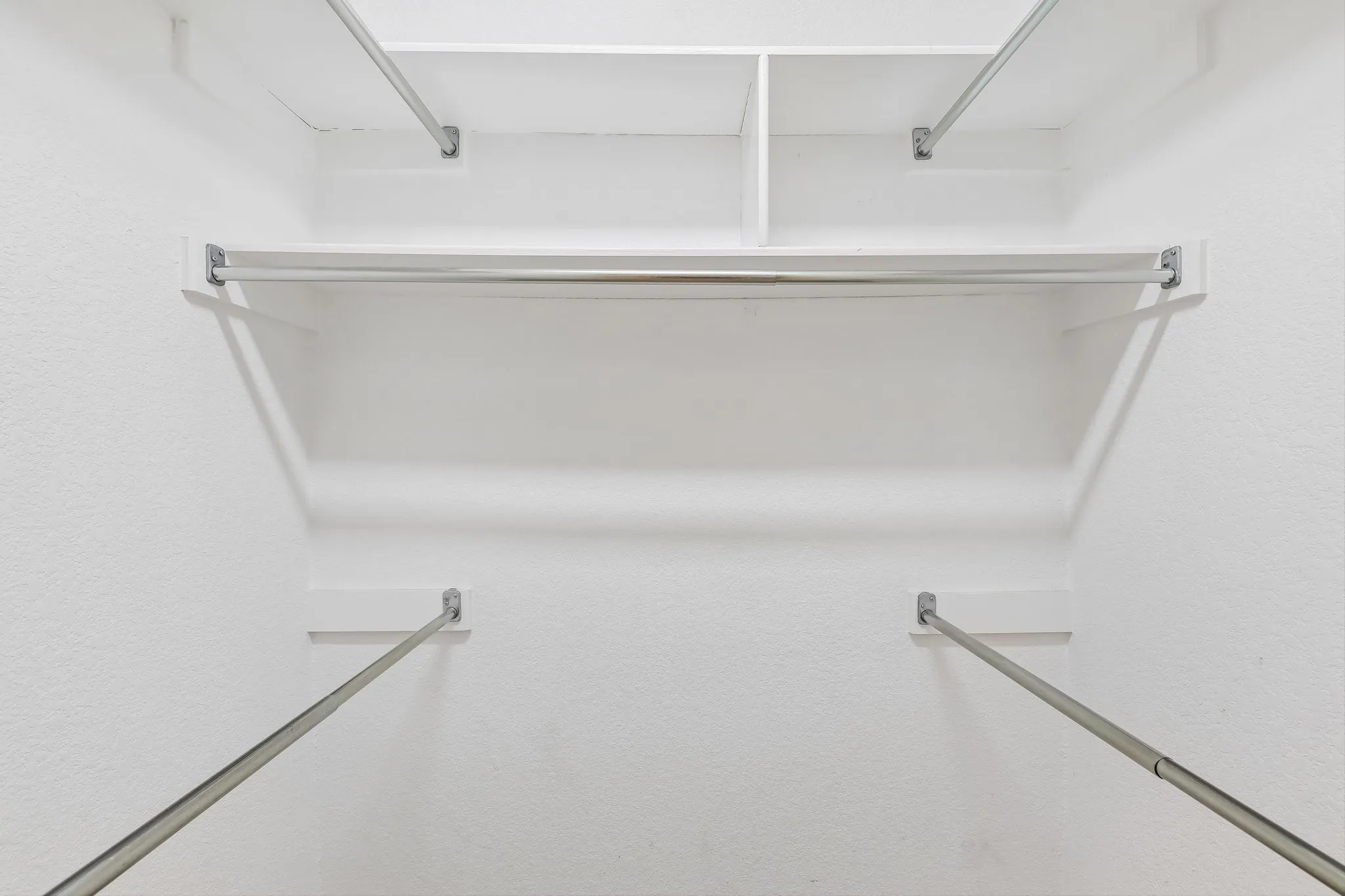 White-painted closet interior featuring built-in shelving, multiple hanging rods, and textured walls
