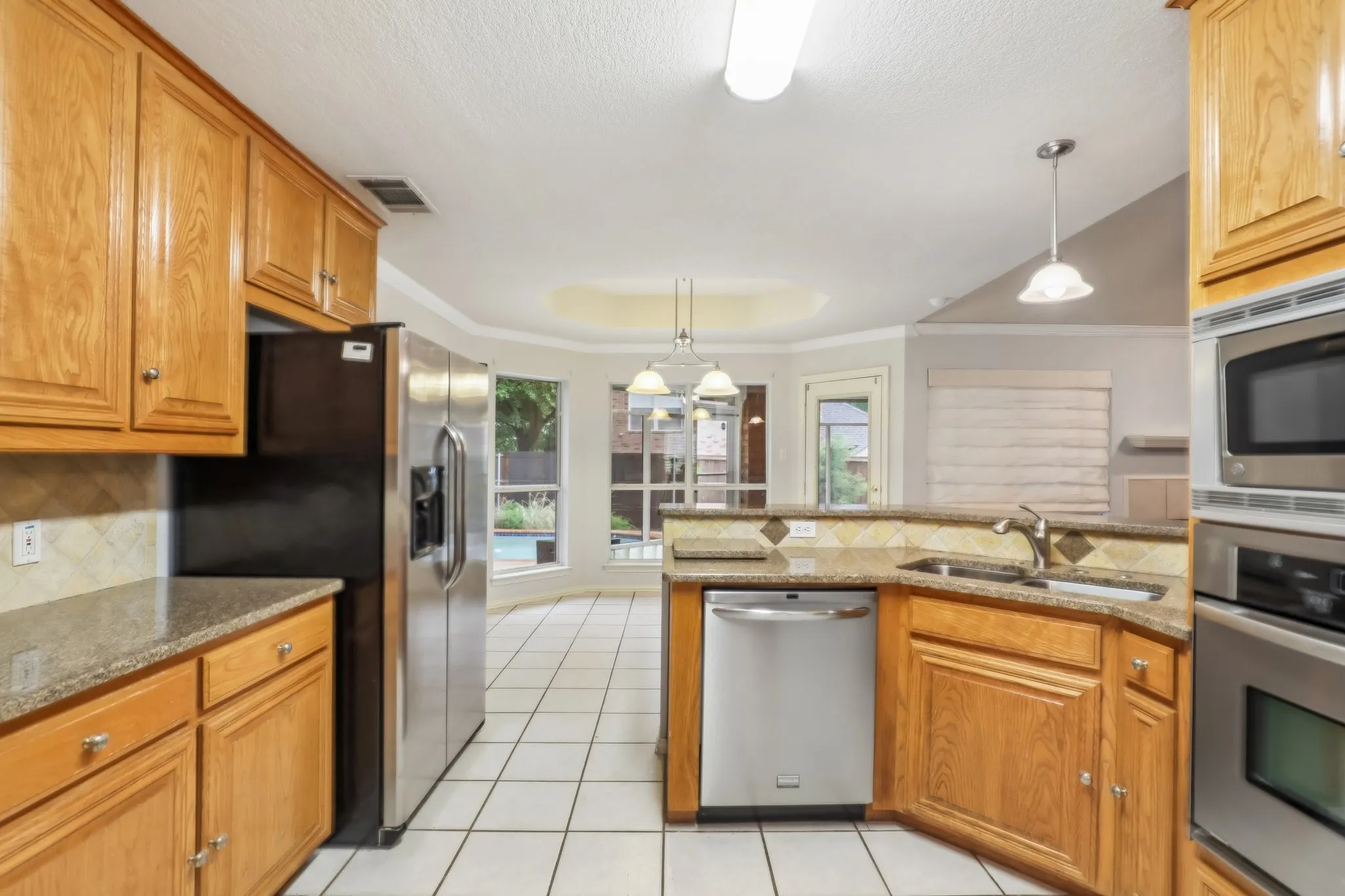 Kitchen featuring light wood cabinetry, granite countertops, stainless steel appliances, and tile flooring
