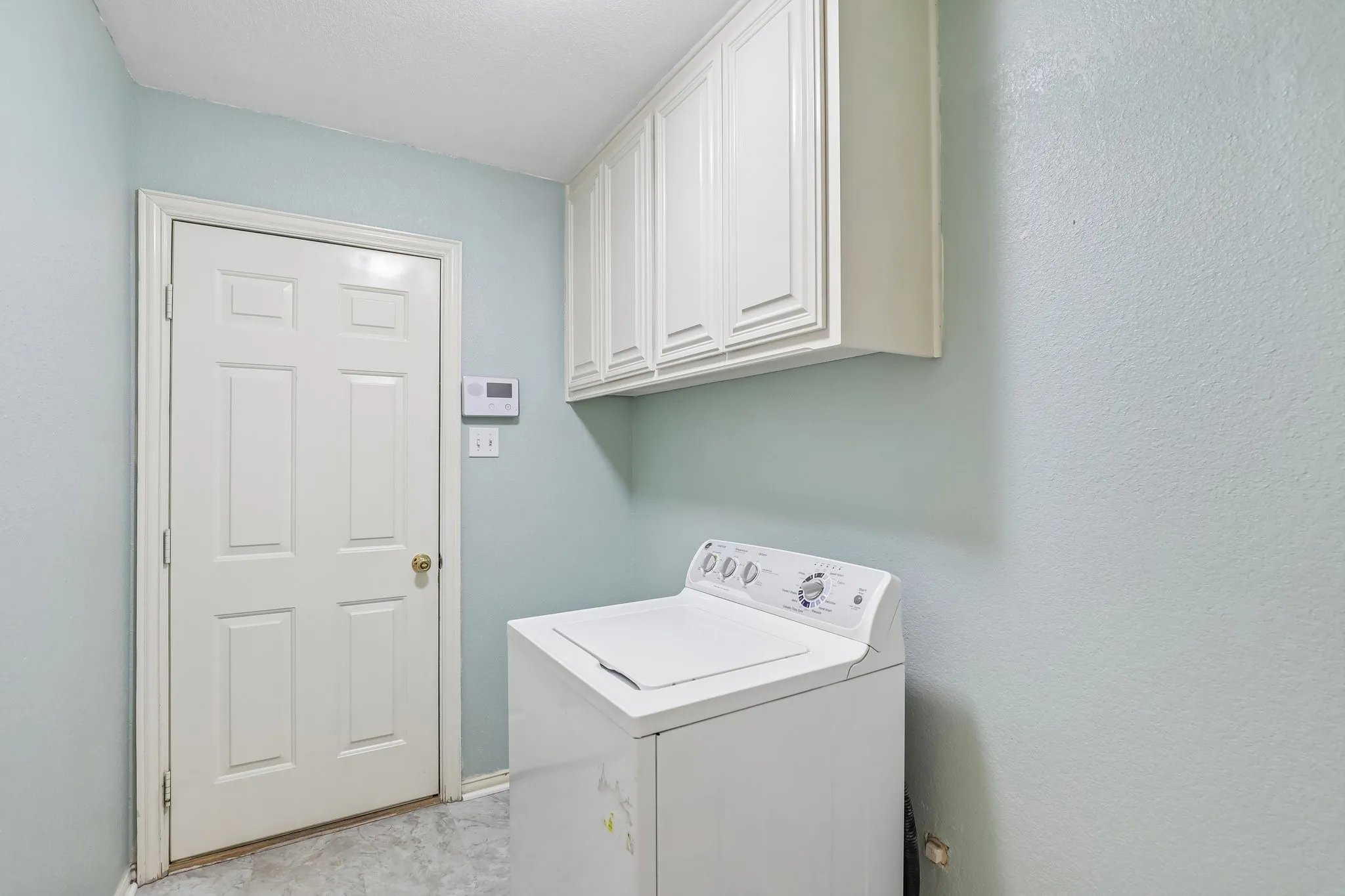 Laundry area featuring overhead cabinetry, light blue wall paint, and a six-panel interior door