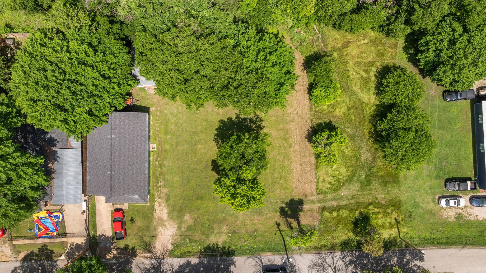 Aerial perspective highlighting a property with a dark shingle roof, surrounded by mature trees