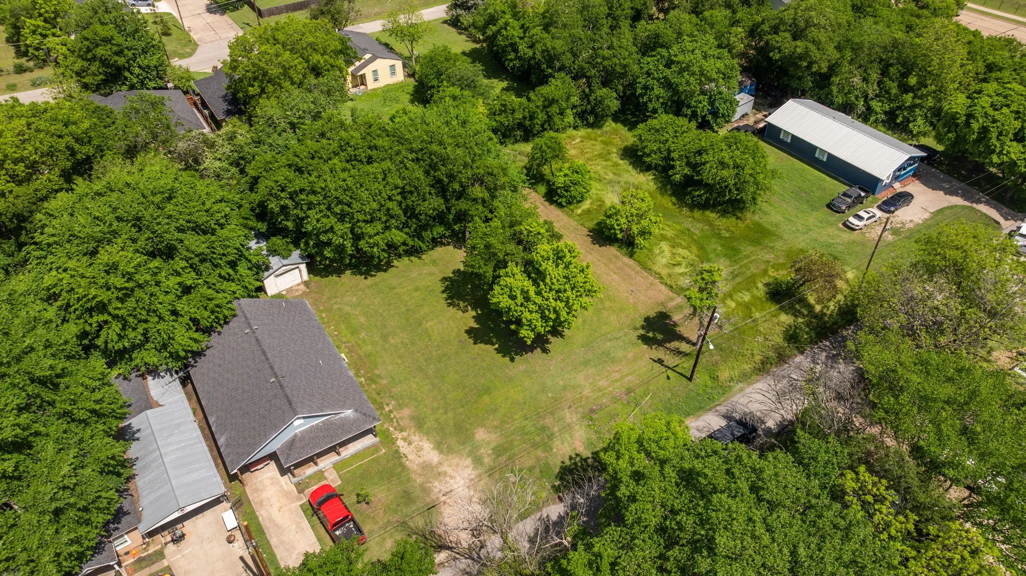 Expansive lot featuring a residential structure with a dark shingle roof, a detached garage, and a large open green space