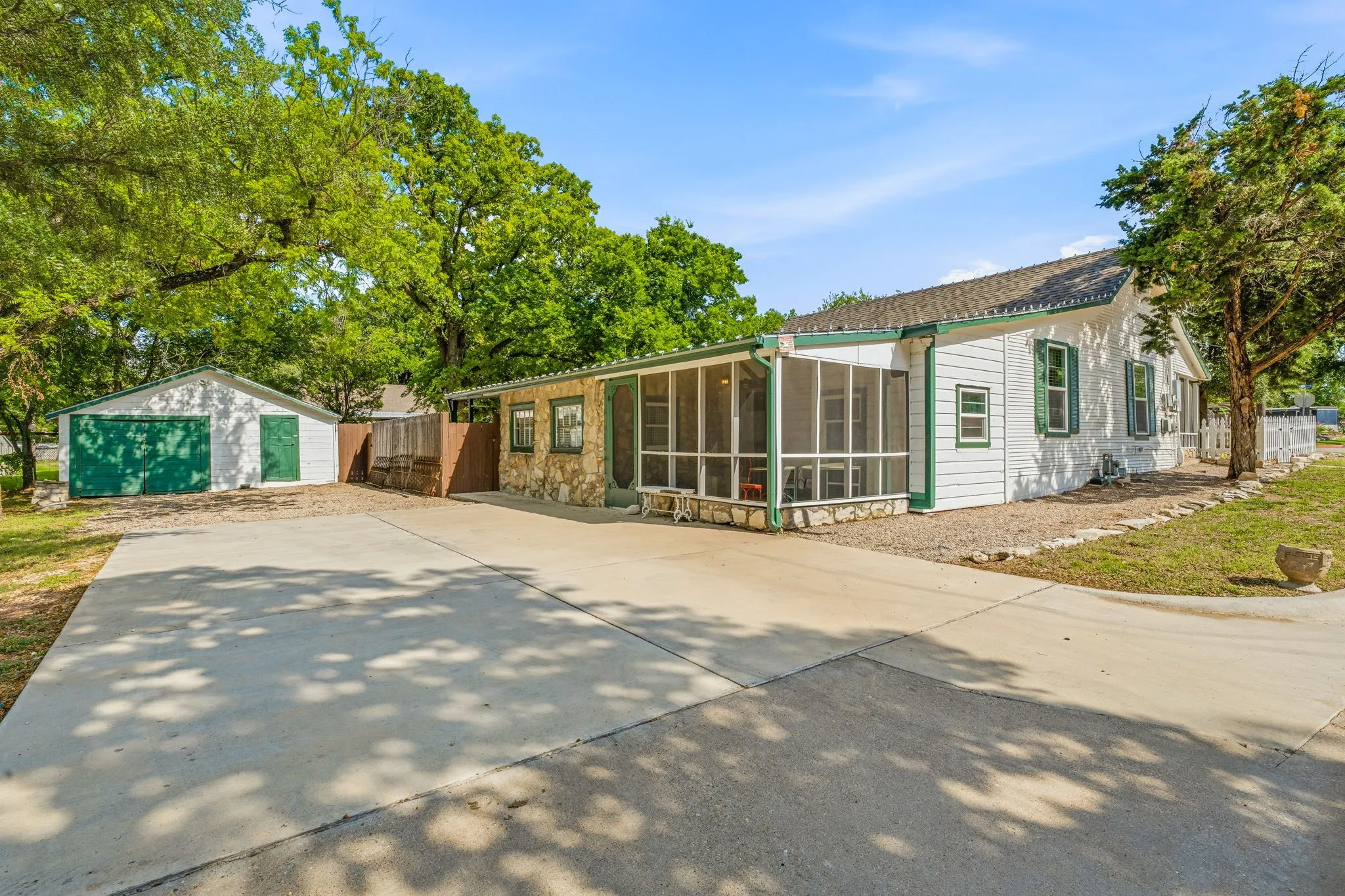 Concrete driveway providing access to a detached garage and a main structure featuring white siding, green shutters, and a screened porch