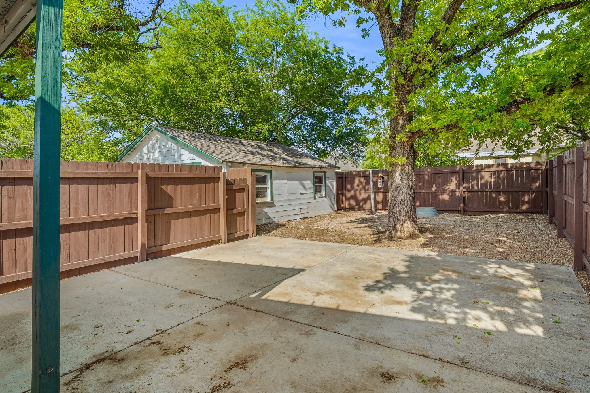 Private backyard featuring concrete patio, gravel landscaping, a mature tree, and wood fencing