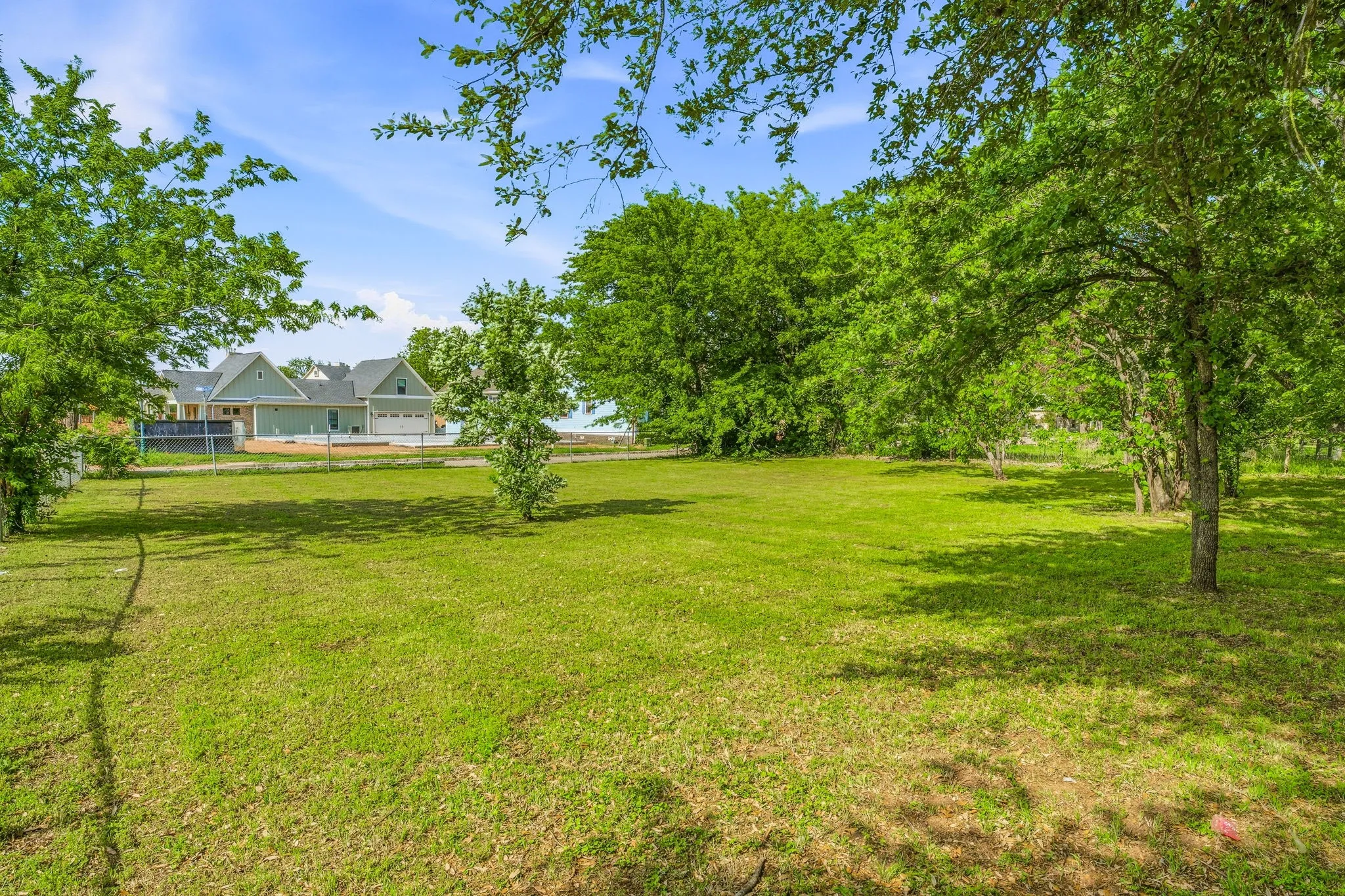 Expansive green lawn with mature trees and a distant dwelling