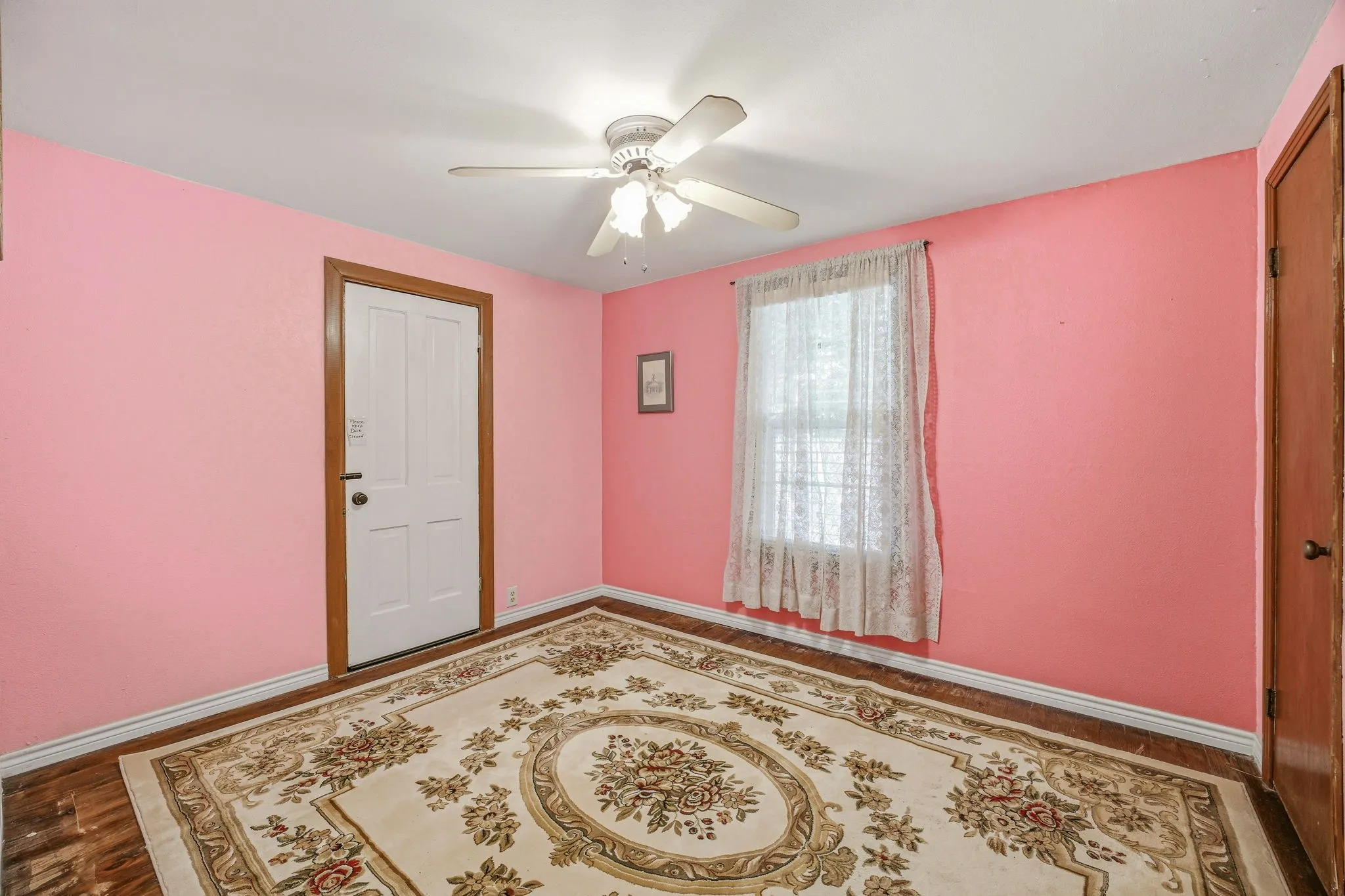 Interior room featuring a white door with wood trim, a window with lace curtains, and light pink walls