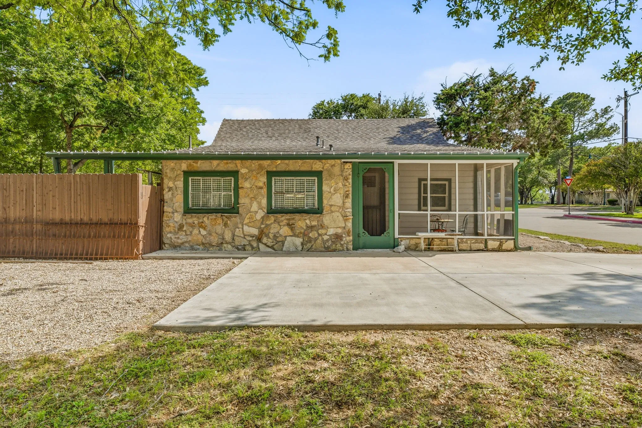 Stone exterior with a screened porch, a paved driveway, a gravel parking area, and a wood privacy fence