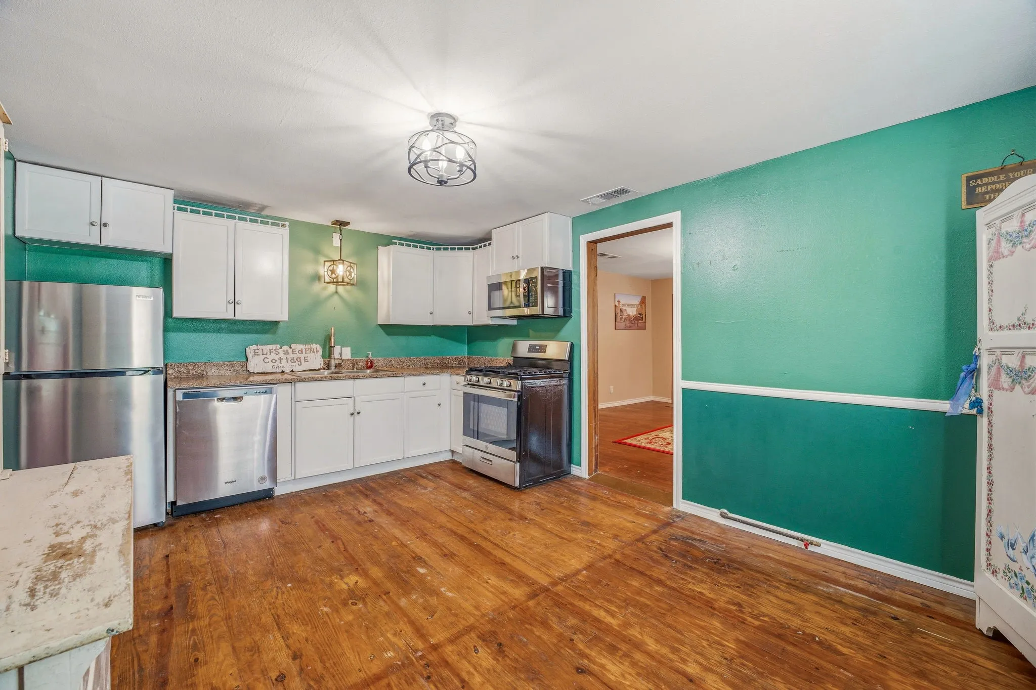 Kitchen featuring wood-finish flooring, white cabinetry, stainless steel appliances, and a decorative ceiling light fixture