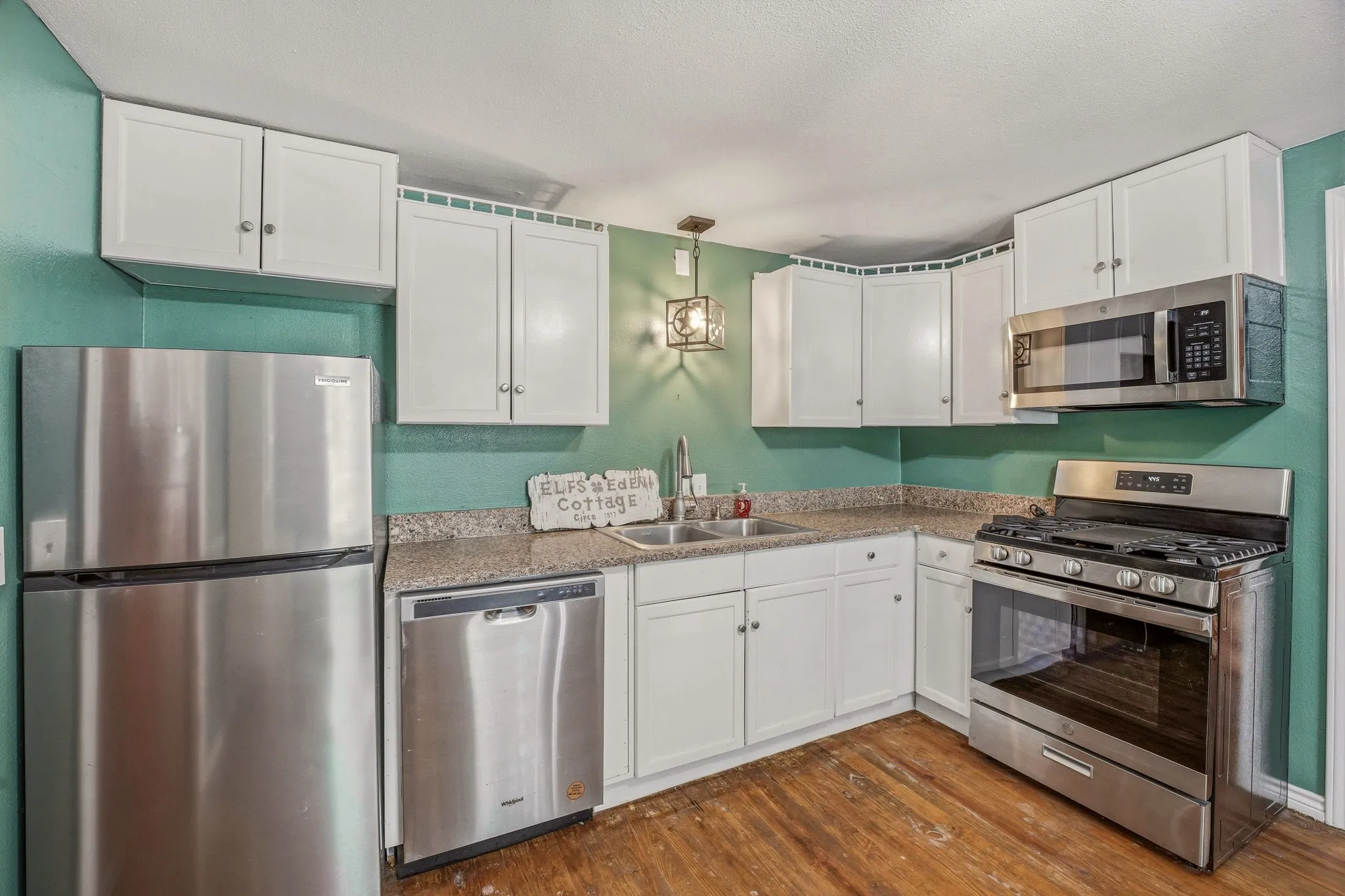 Kitchen featuring white cabinetry, wood-finish flooring, stainless steel appliances, and speckled countertops