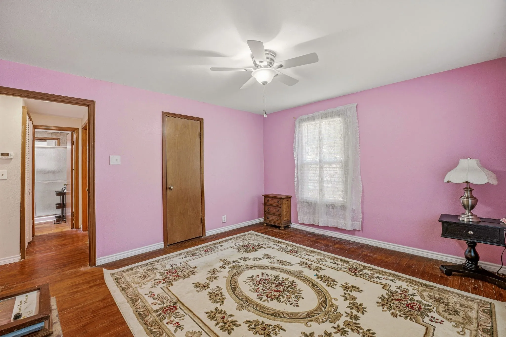 Room featuring wood-finish flooring, a ceiling fan, and a window with sheer curtains