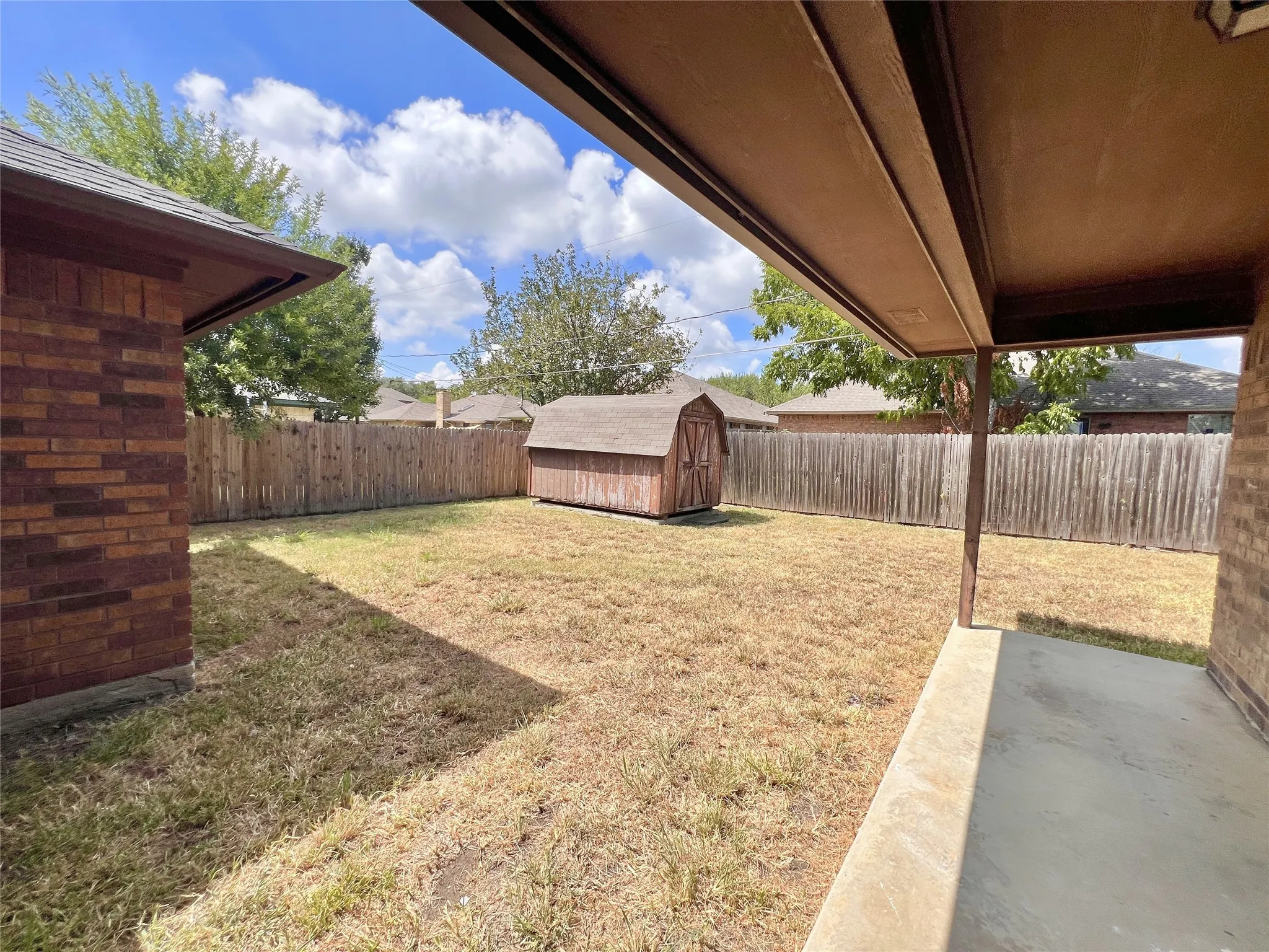 Expansive backyard featuring a privacy fence, covered patio, and a storage shed. These pictures are prior to the current tenant moving in.