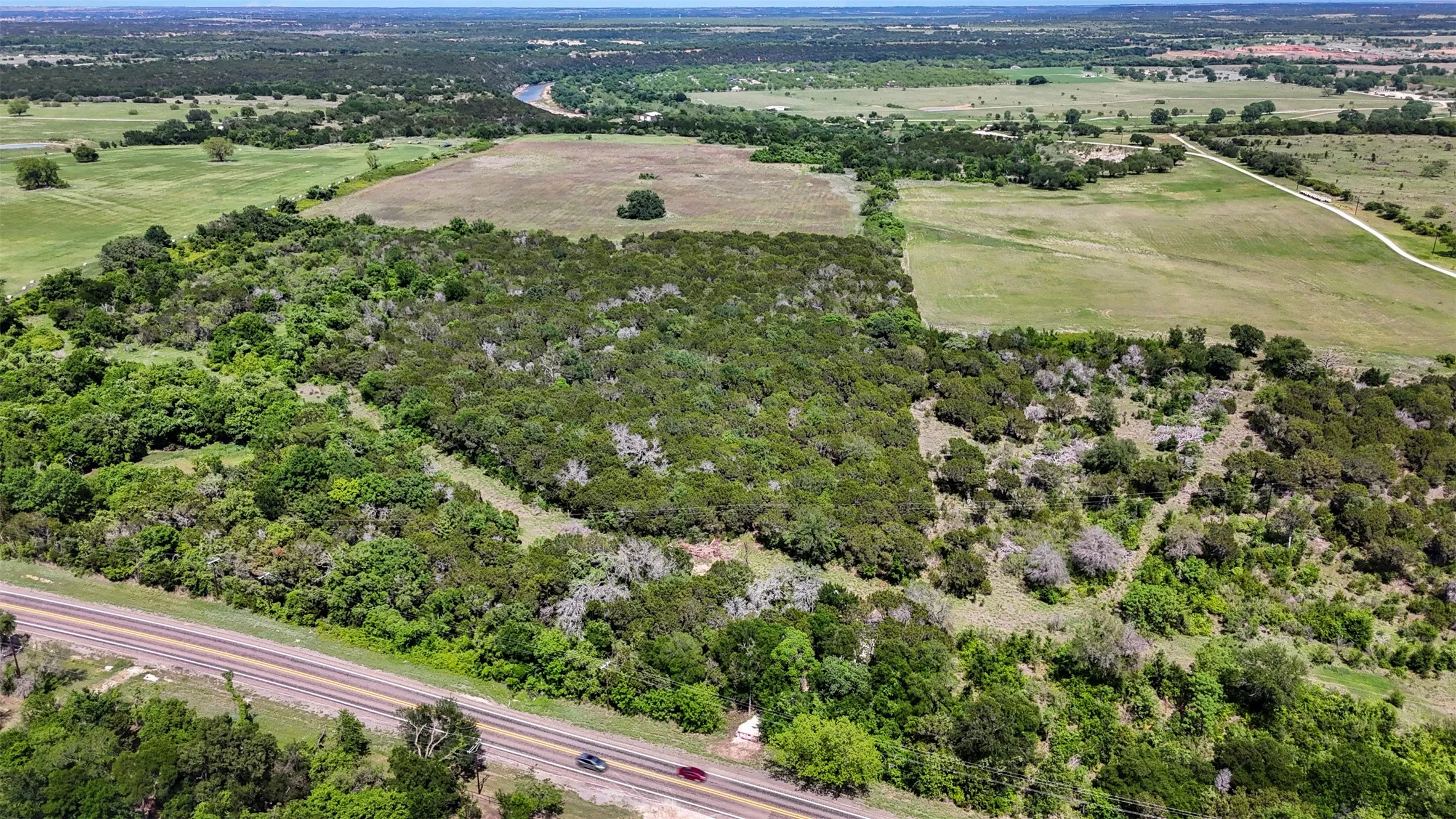 Expansive rural acreage featuring abundant mature trees, a defined boundary with open fields, and direct road frontage