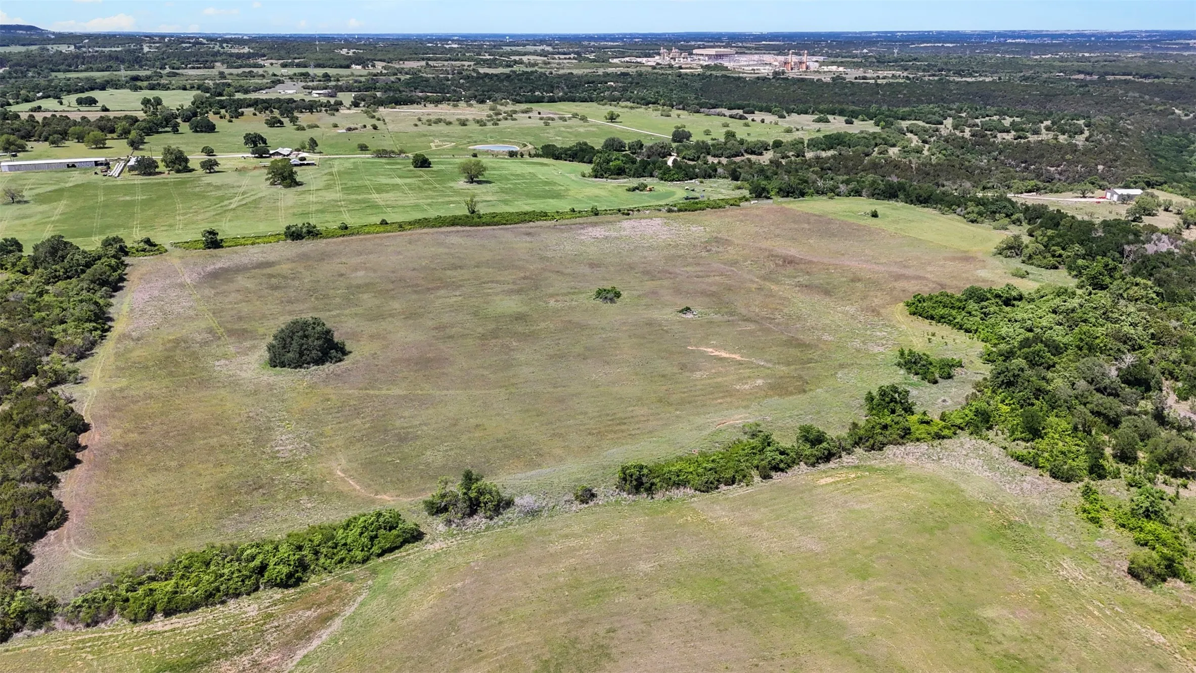 Expansive agricultural land featuring a central tree cluster and perimeter greenery