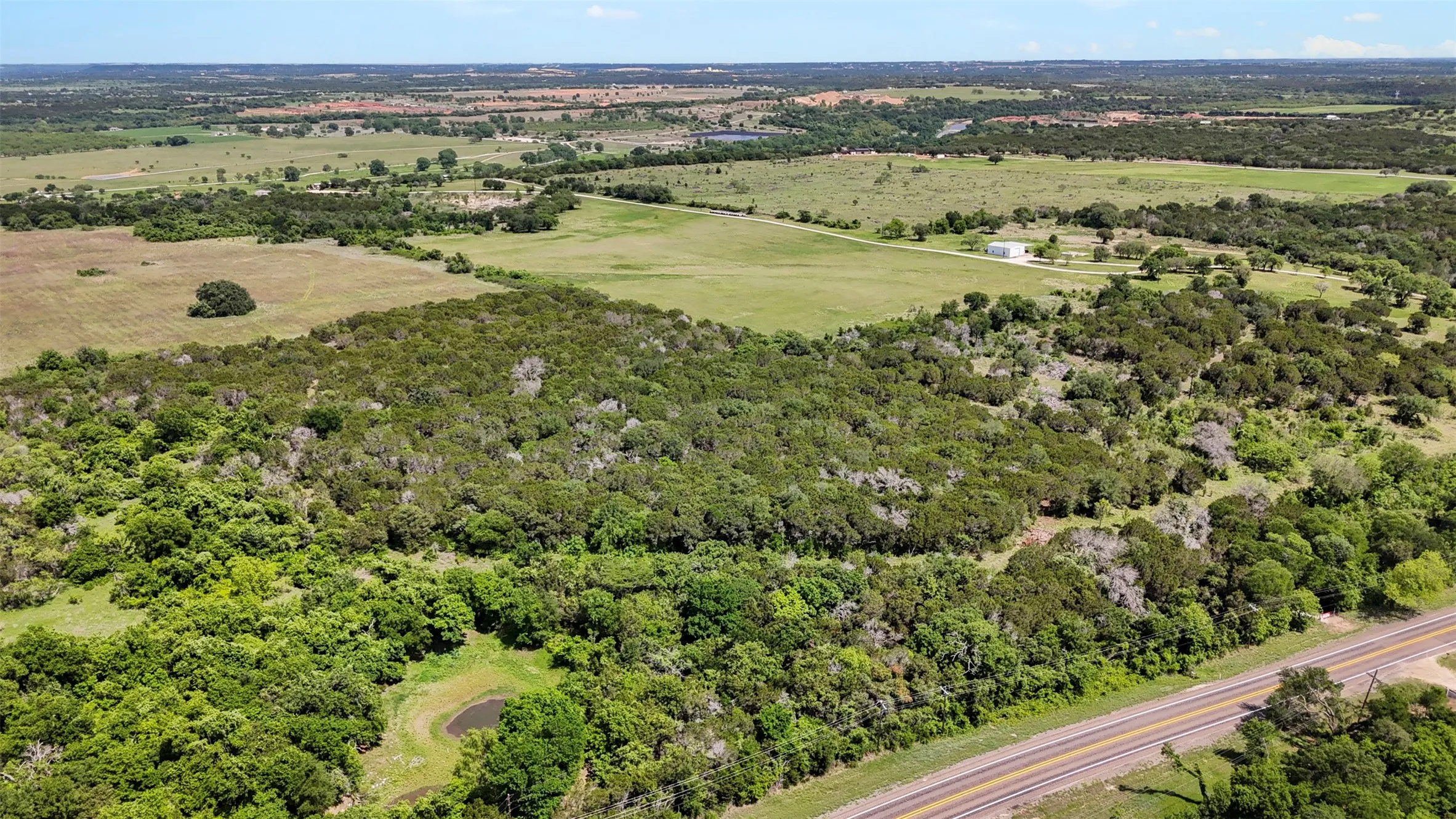 Expansive acreage featuring dense tree coverage, open grassy areas, and a natural pond