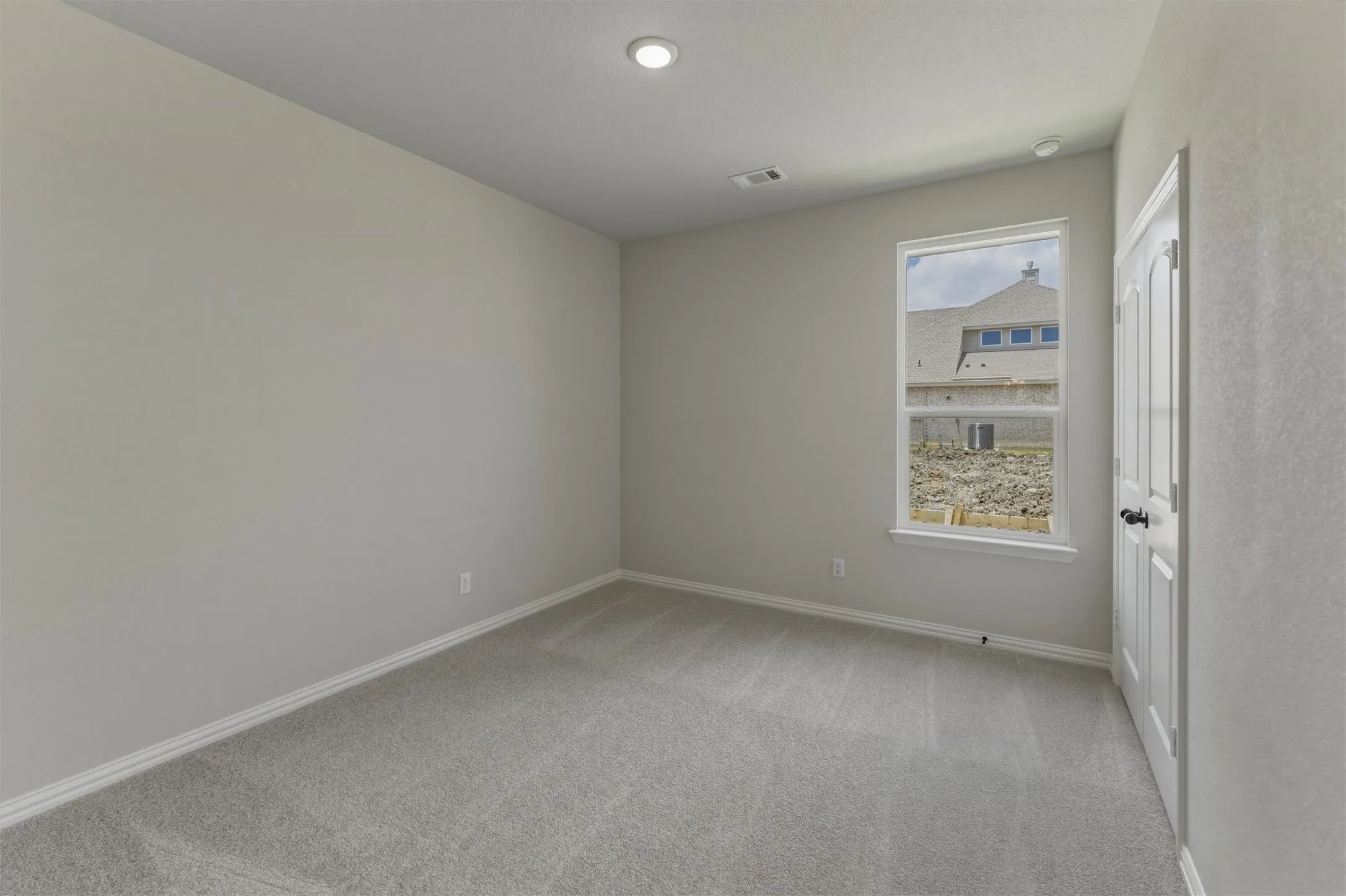 Neutral-toned interior room featuring light gray carpeting, white baseboards, and a single window with white trim