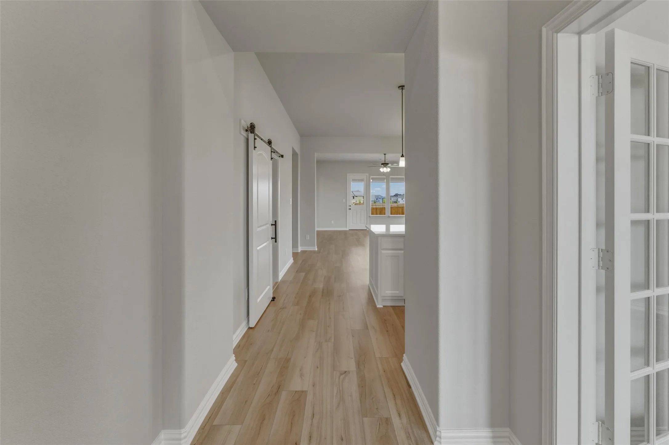 Interior hallway featuring wood-finish flooring, white baseboards, and a barn door with black hardware