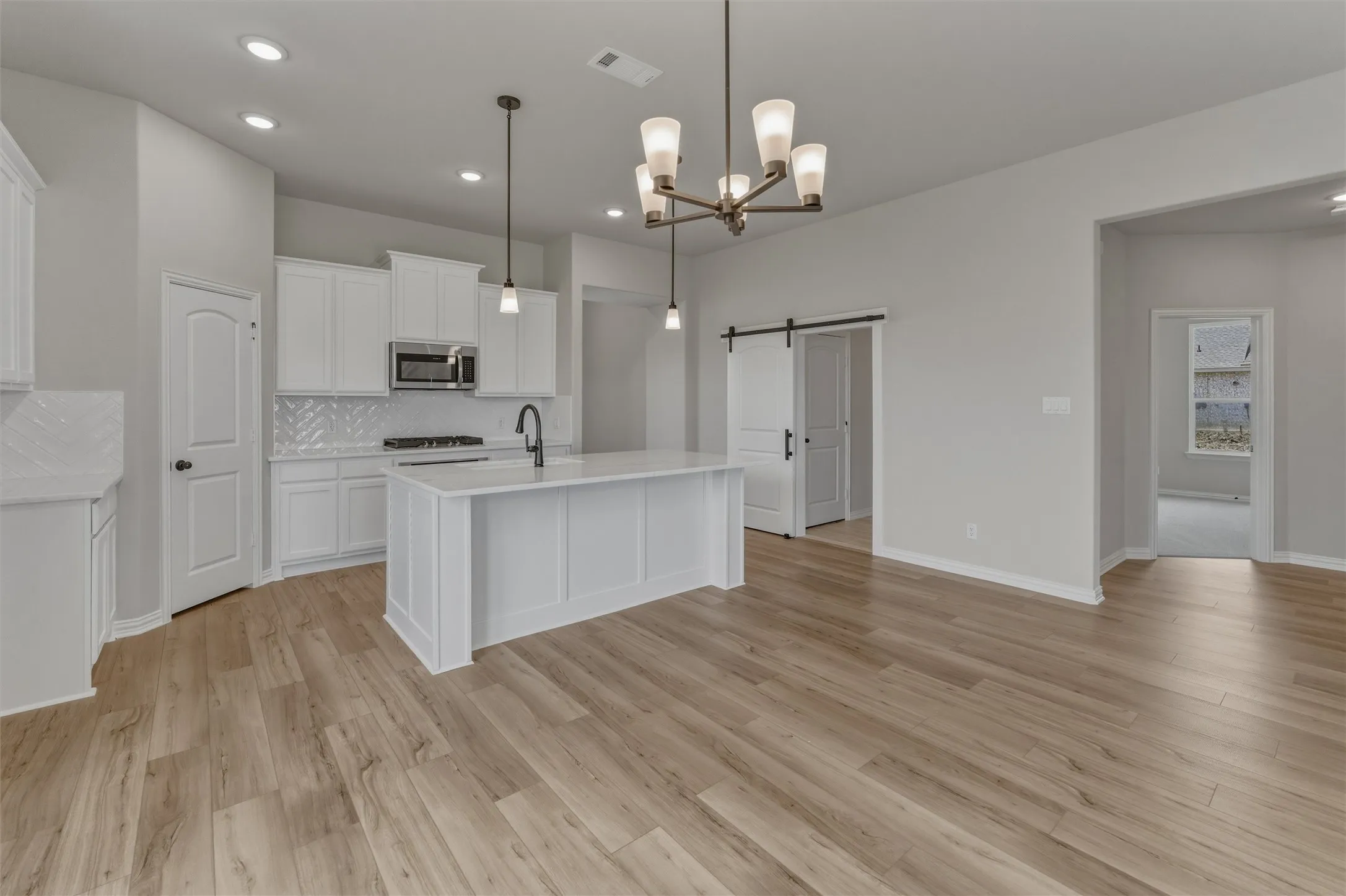 Open-concept kitchen featuring white cabinetry, a central island, stainless steel appliances, a tile backsplash, and wood-finish flooring