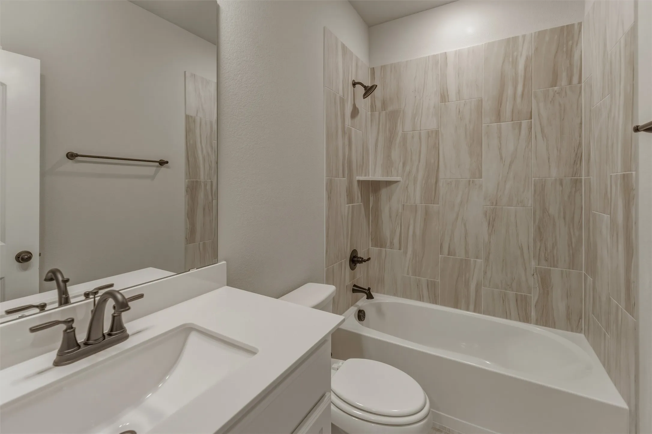Bathroom featuring a white vanity with a rectangular sink and solid surface countertop, bronze finish plumbing fixtures, a full-width mirror, and a shower-over-tub with tiled surround