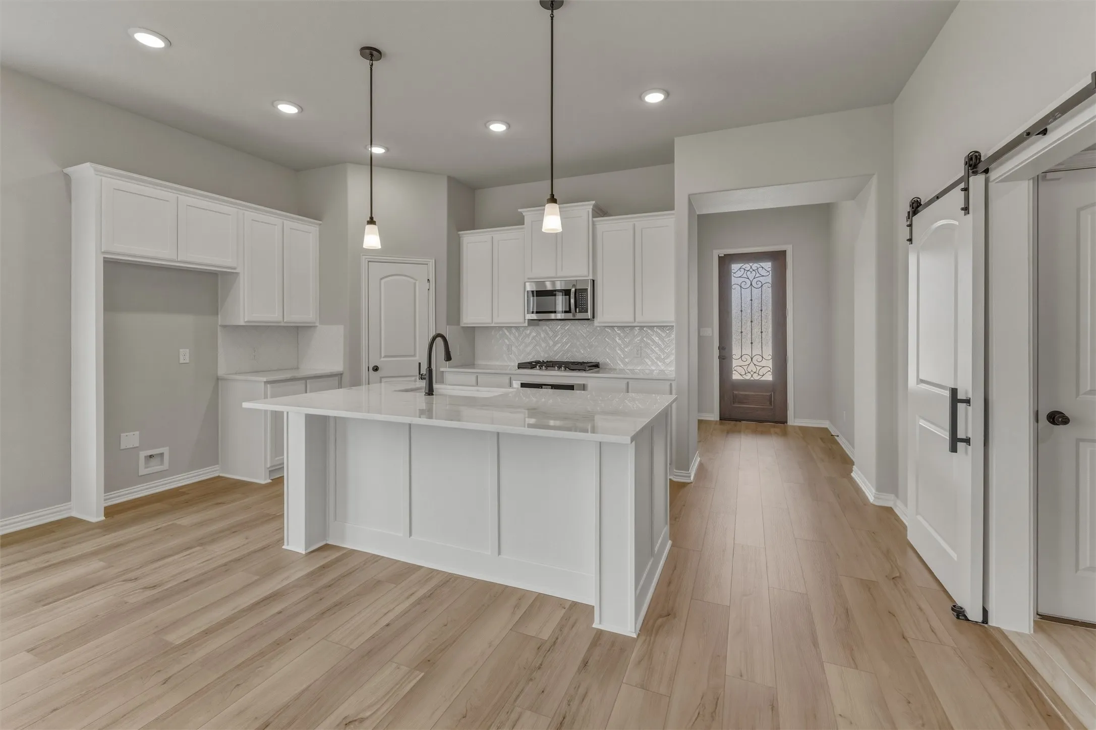 Modern kitchen featuring a central island with countertop seating, white shaker cabinetry, herringbone tile backsplash, and light wood-finish flooring