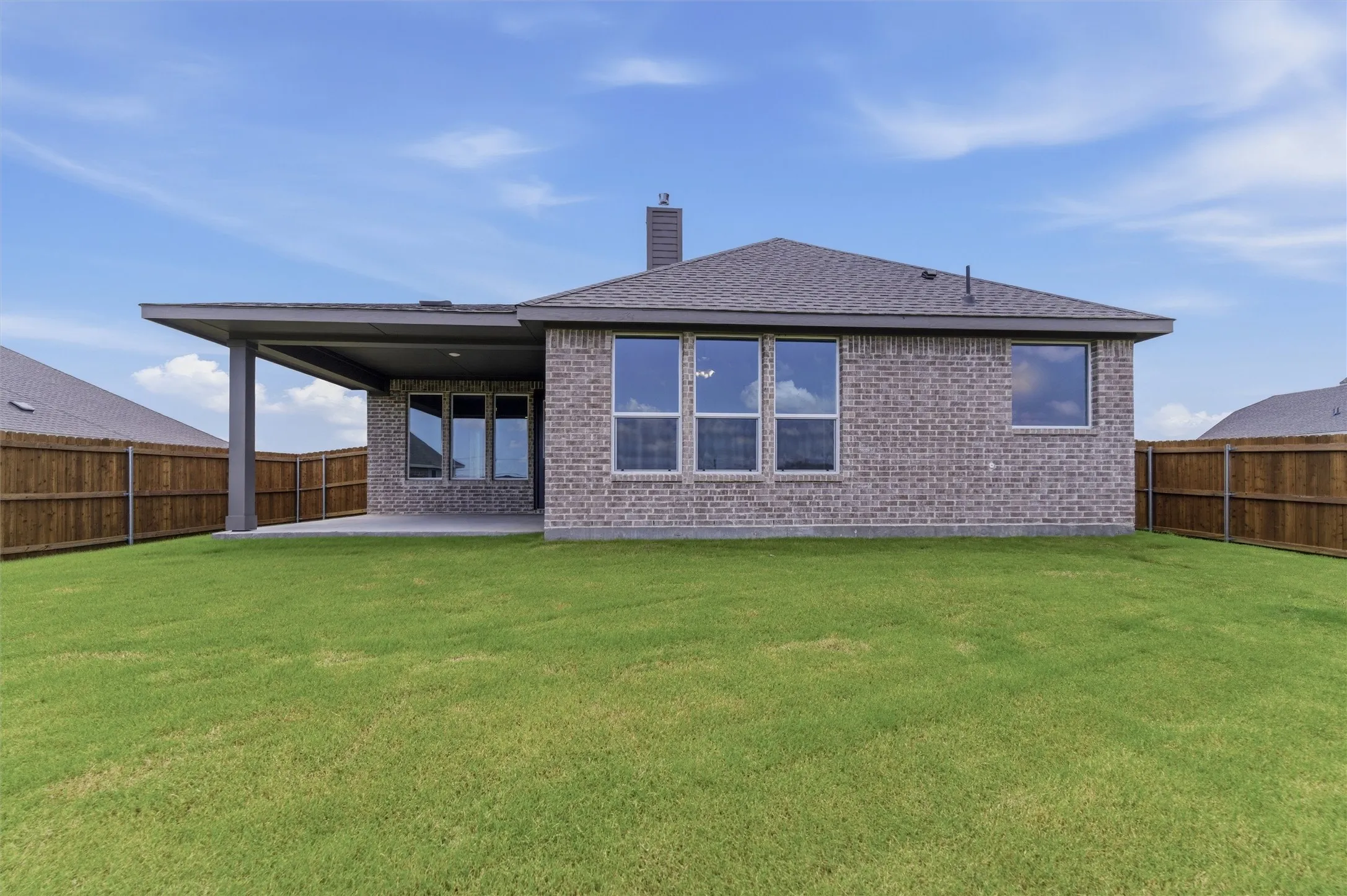 Expansive backyard featuring a manicured lawn, full privacy fencing, and a covered patio