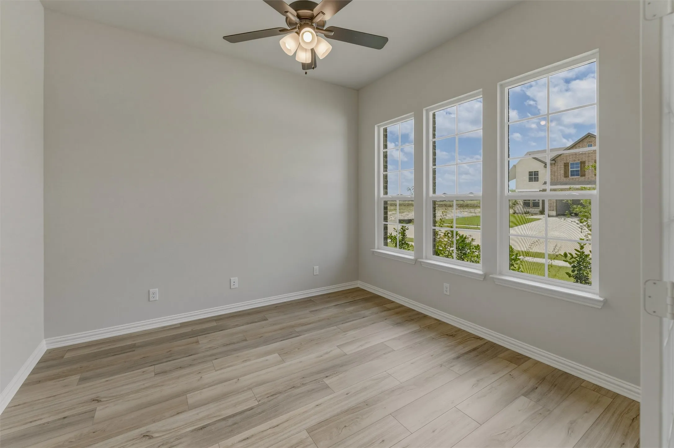 Room with three large windows, wood-finish flooring, and a ceiling fan