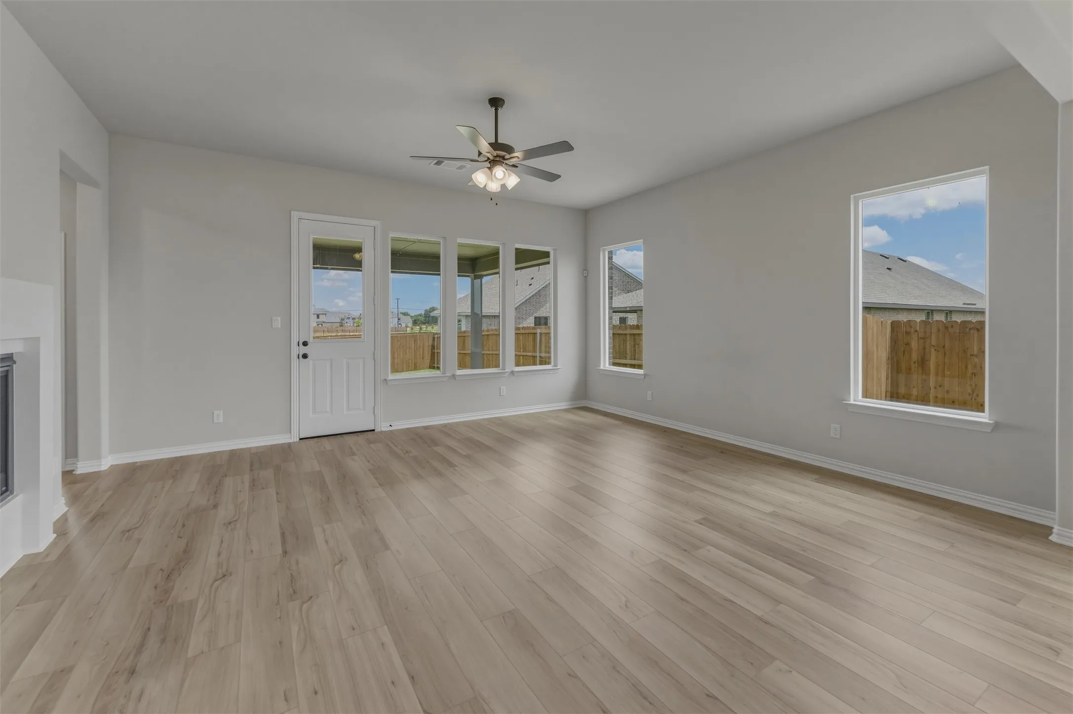 Spacious living area featuring contemporary wood-finish flooring, a ceiling fan with integrated lighting, and multiple windows for abundant illumination