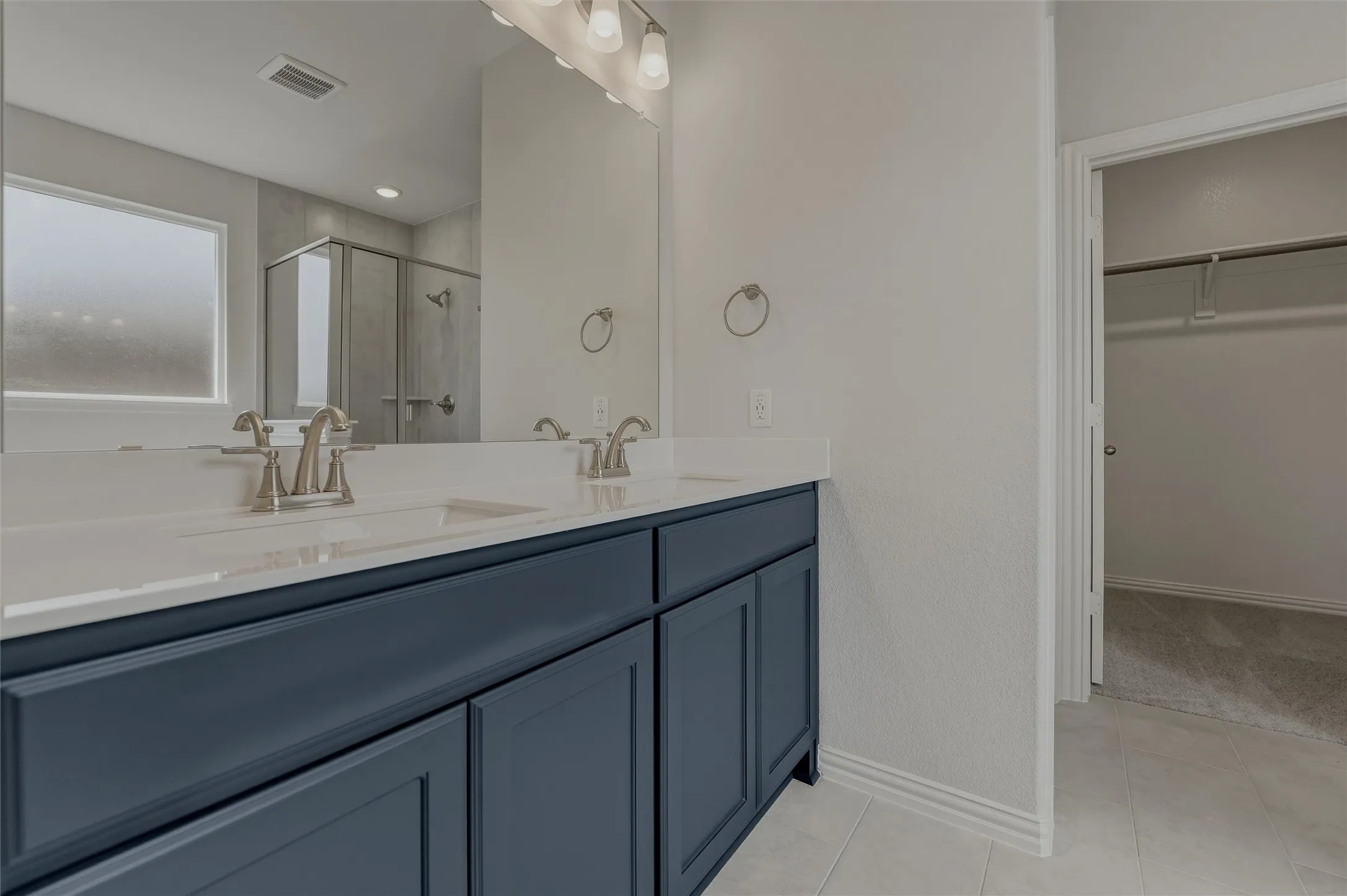 Dual vanity with dark blue cabinetry and white countertops, large mirror, and shower enclosure with glass panels