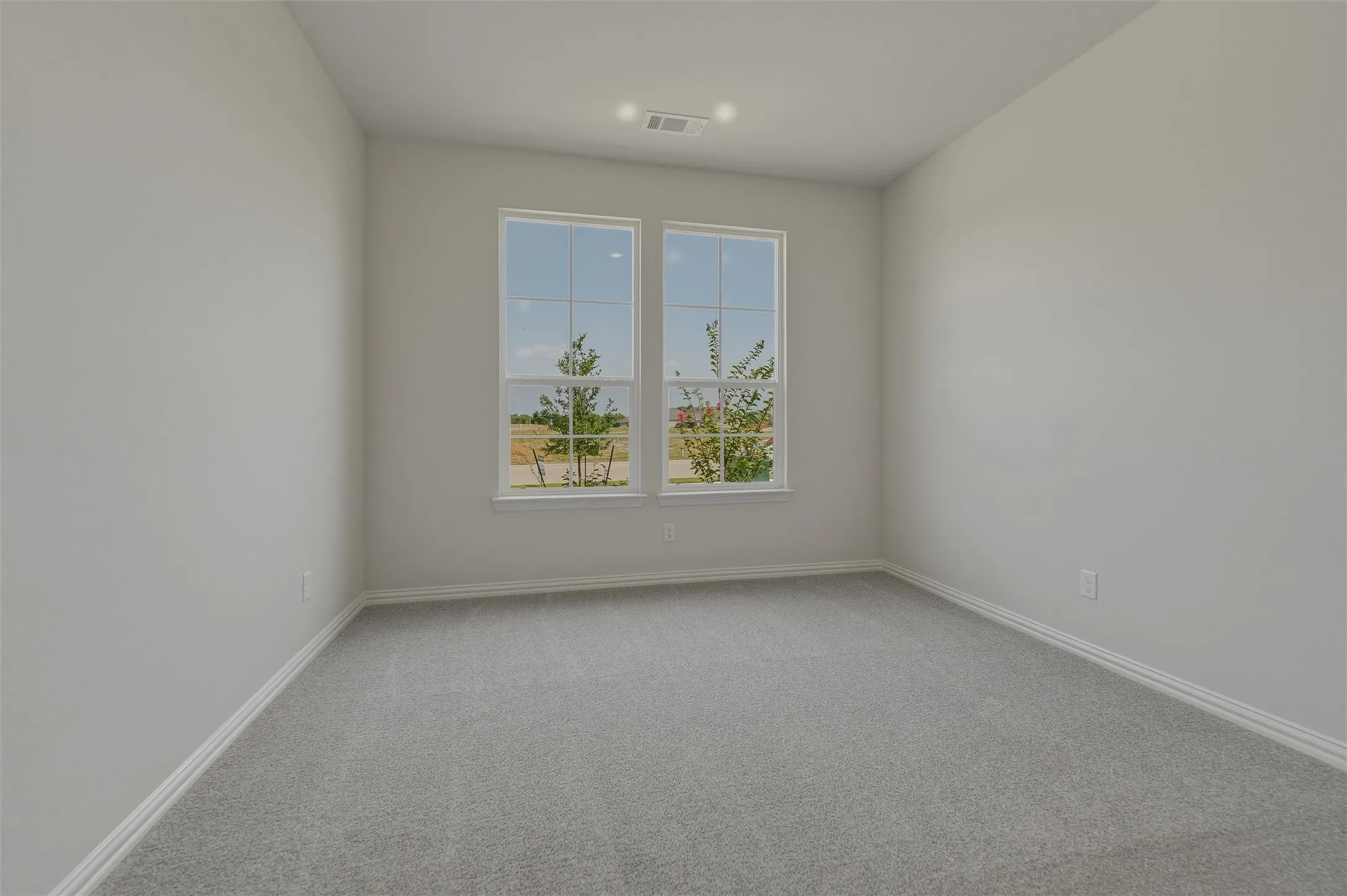 Bright, light-filled bedroom featuring dual casement windows with expansive natural light, neutral wall finishes, and soft gray carpet flooring