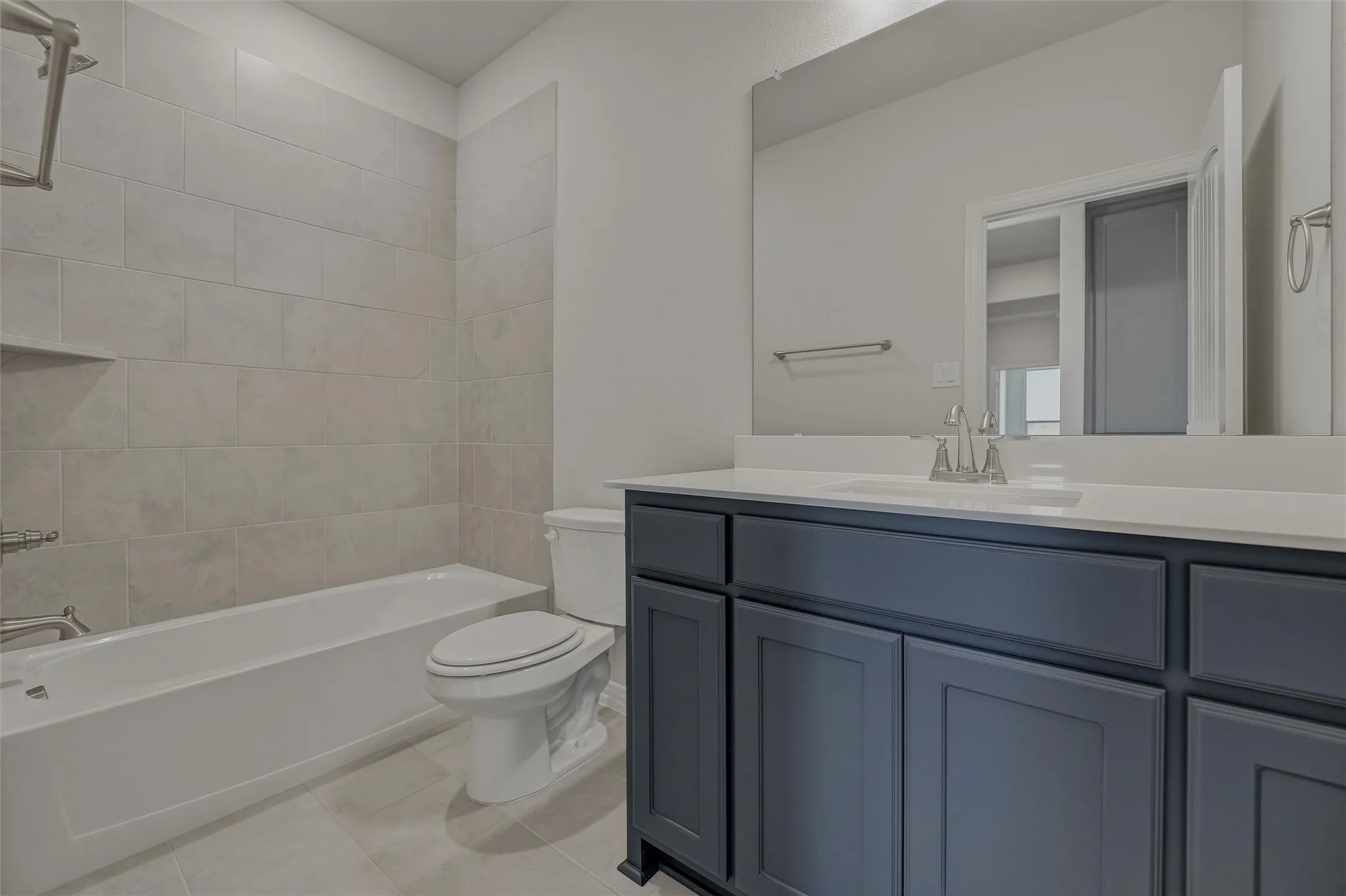 Tub-shower combination with tiled surround, built-in shelving, and a vanity featuring a single sink and cabinet storage