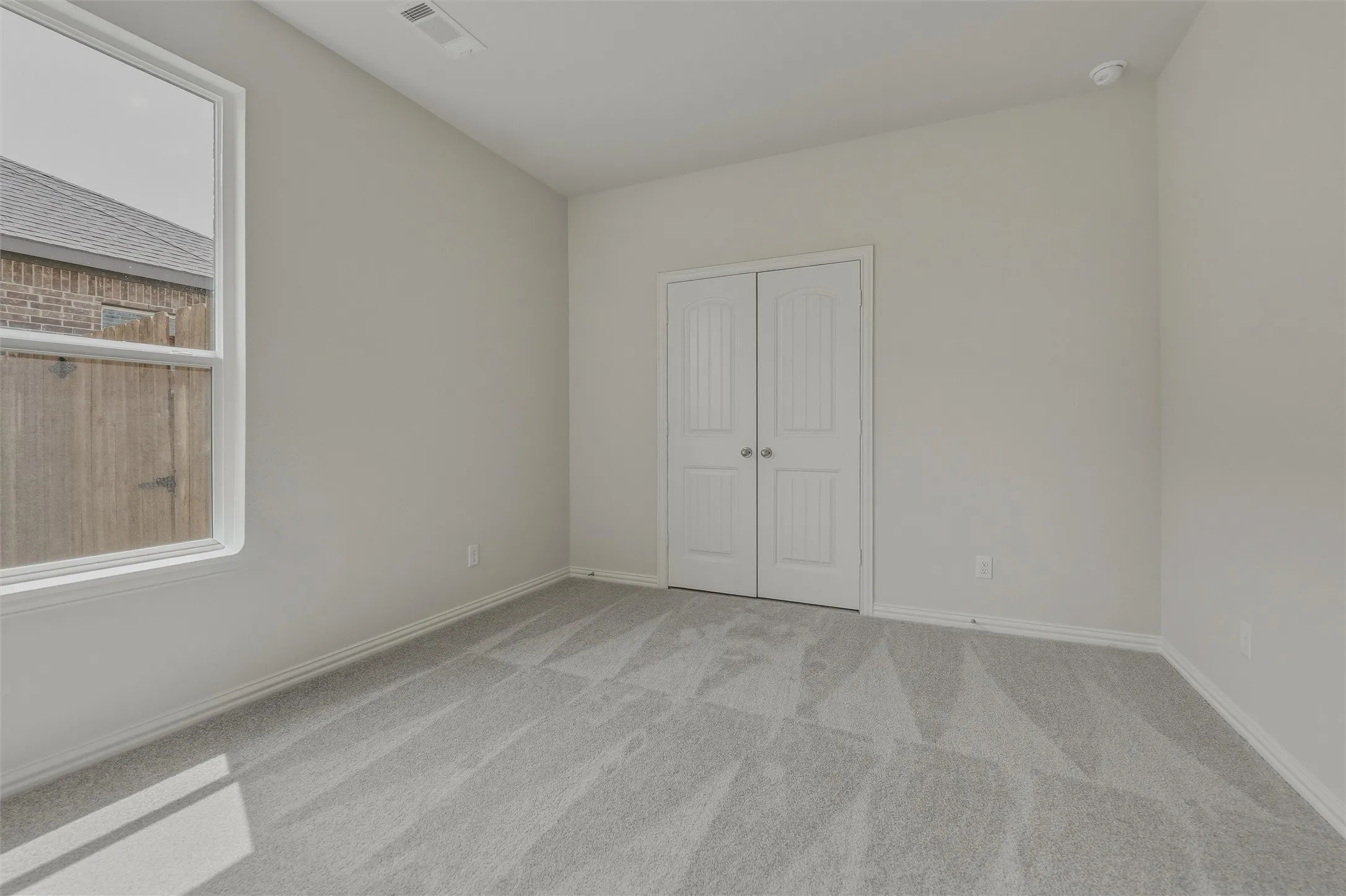 Bright secondary bedroom showcasing plank-style wood-finish flooring, abundant natural light from a large window, and dual closets with white panel doors for ample storage