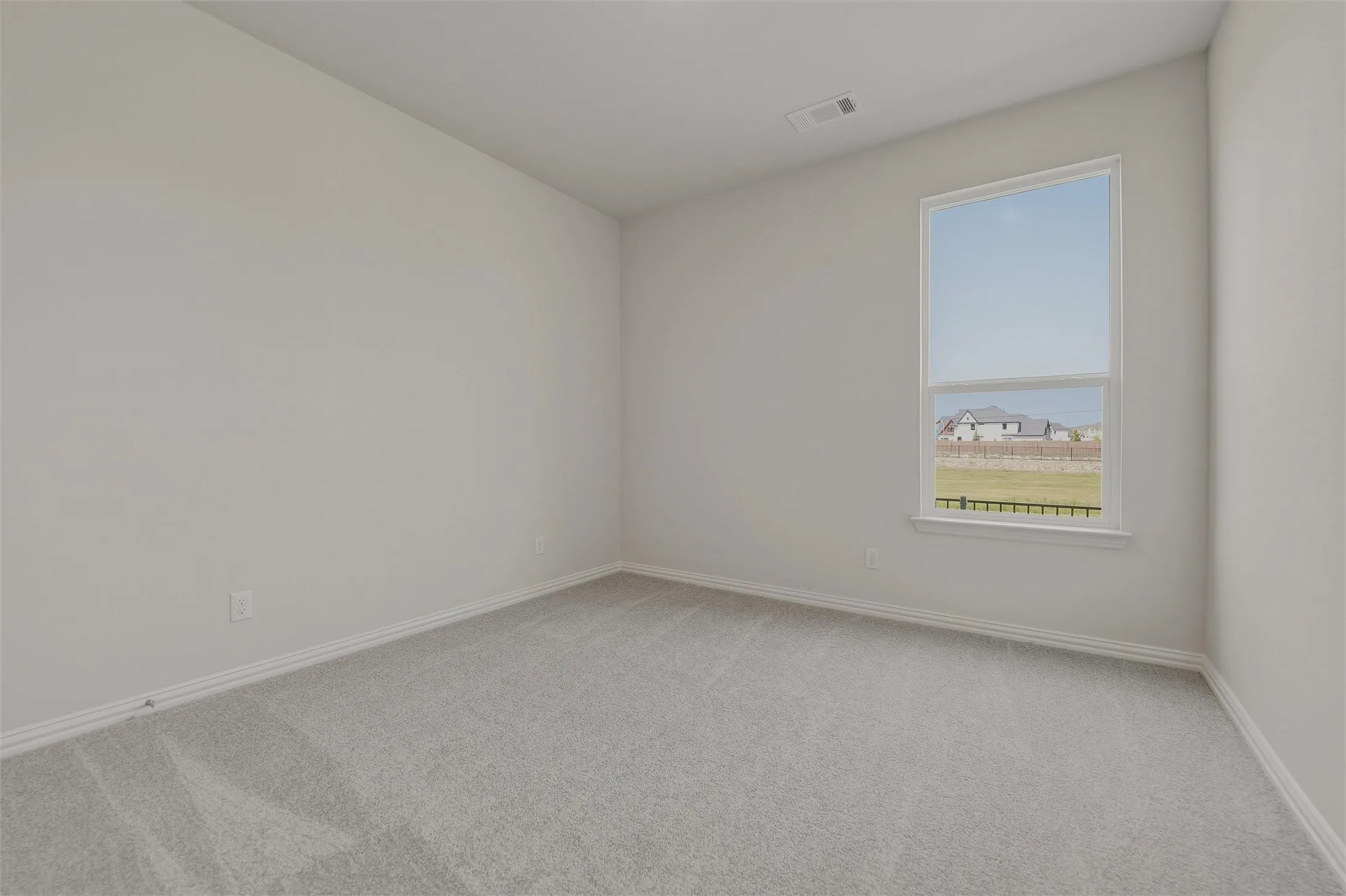 Neutral wall paint, light-colored carpeting, and a large window providing natural illumination
