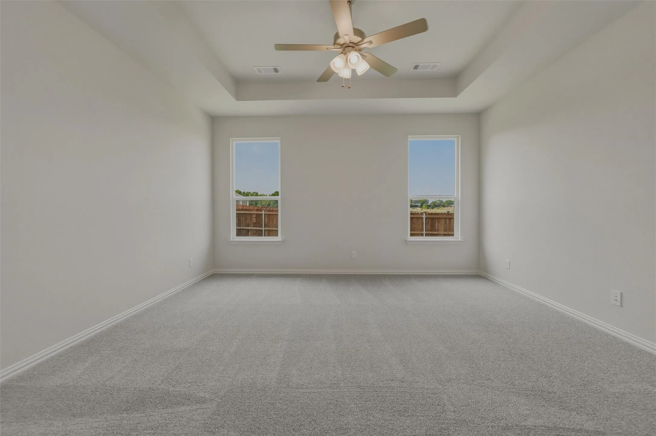 Tray ceiling with a ceiling fan, two windows, and gray carpeting