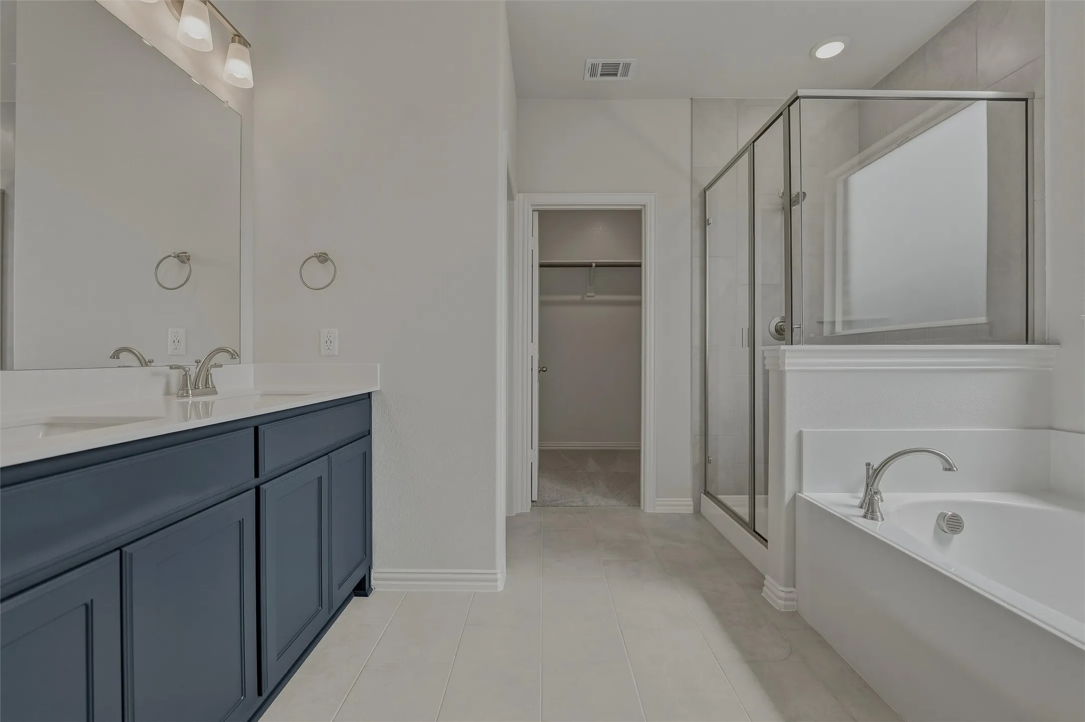 Dual vanity with a stone countertop and undermount sinks, glass-enclosed shower, built-in bathtub, and tile flooring